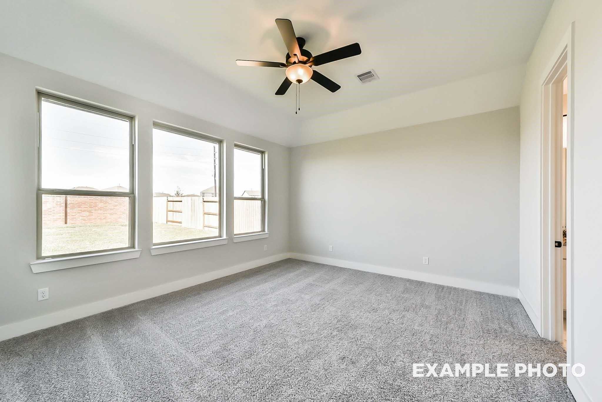 Bright bedroom with three large windows, ceiling fan, and beige carpet in Davidson Homes The Philip C, Rosharon, Texas