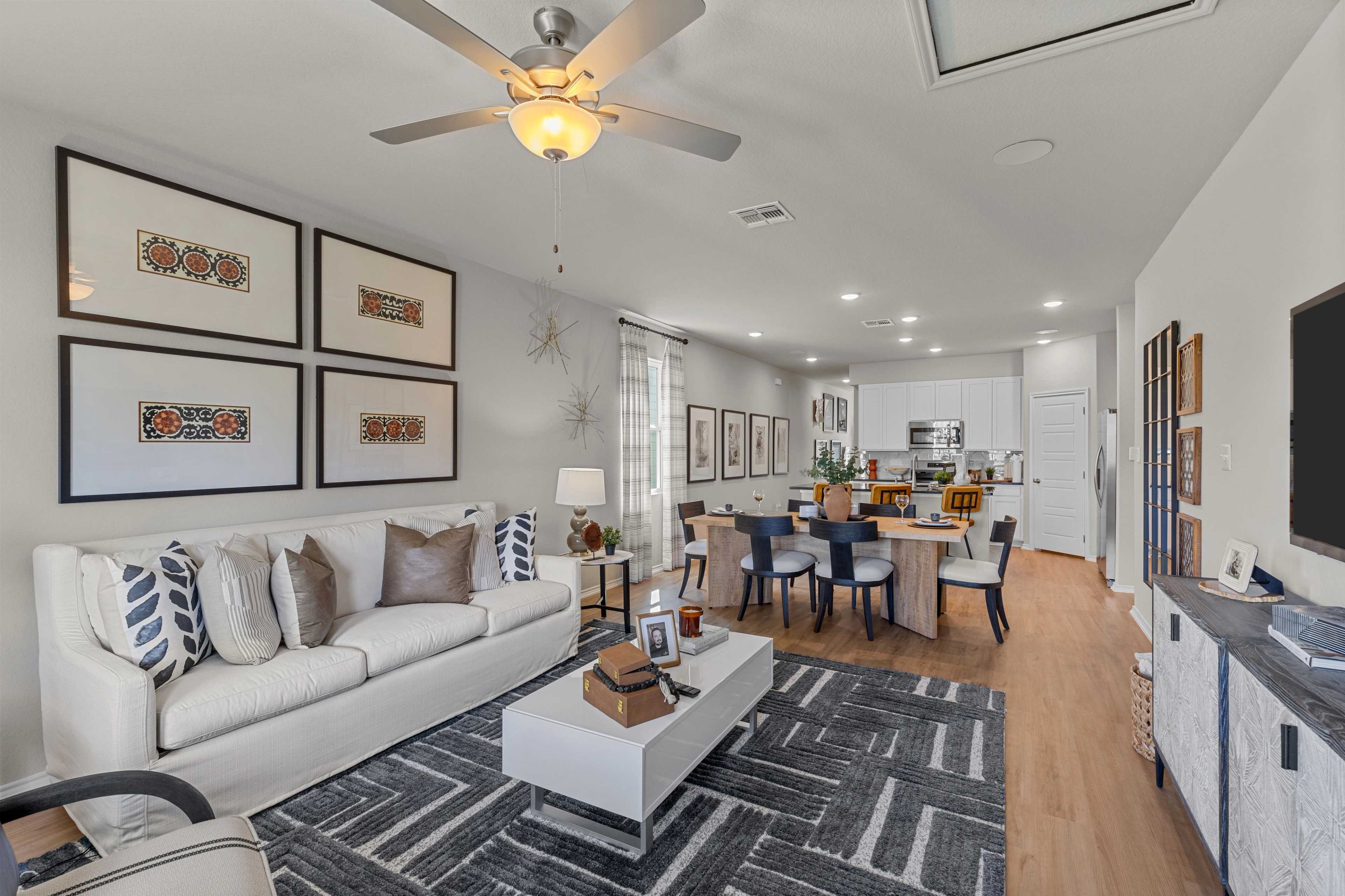 Open-concept living room at Meadows at Oak Creek in San Antonio TX with white sofa, dining table, hardwood floors, modern wall art