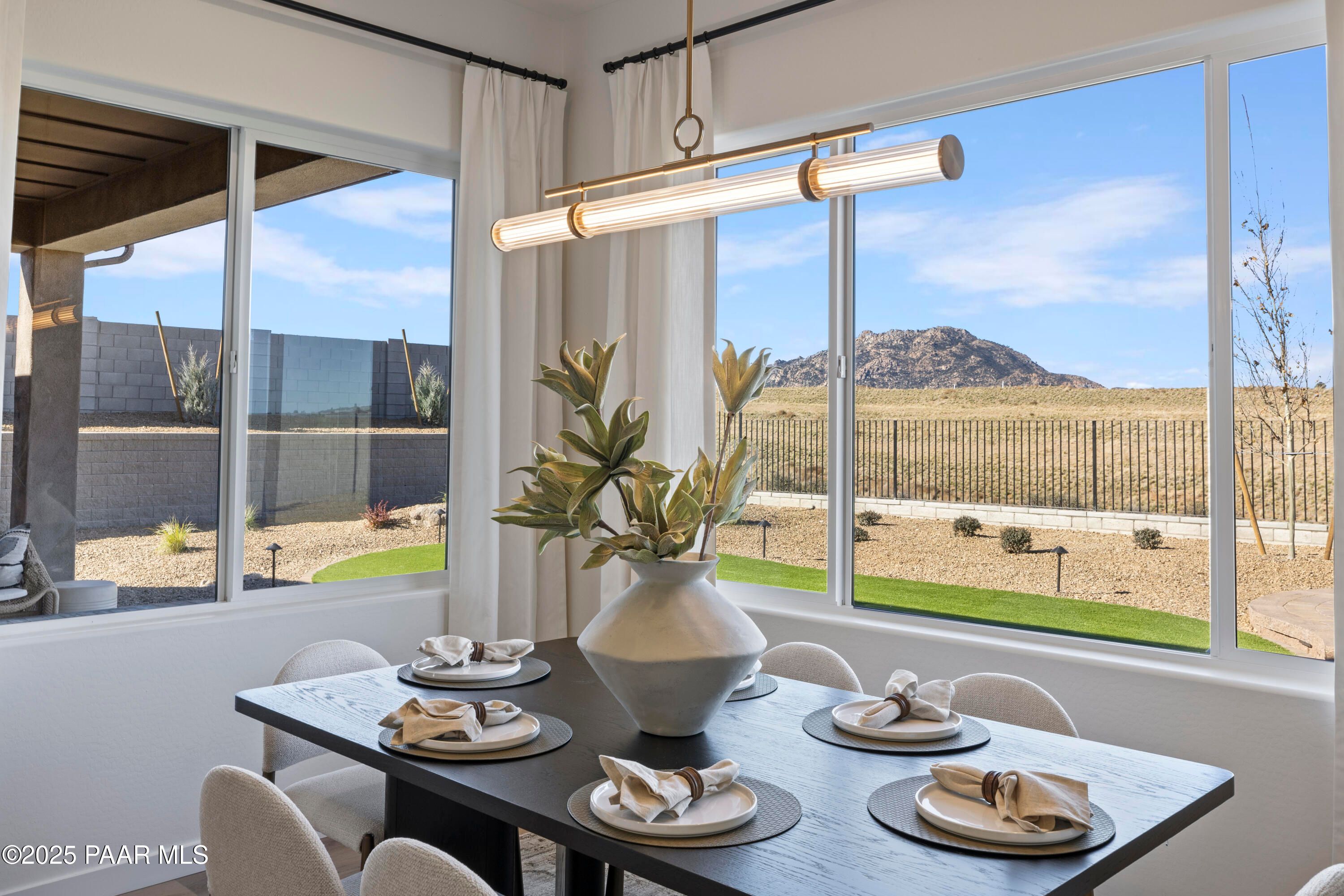 Modern dining area with set table, large potted plant, and desert mountain views through windows in Prescott, AZ home