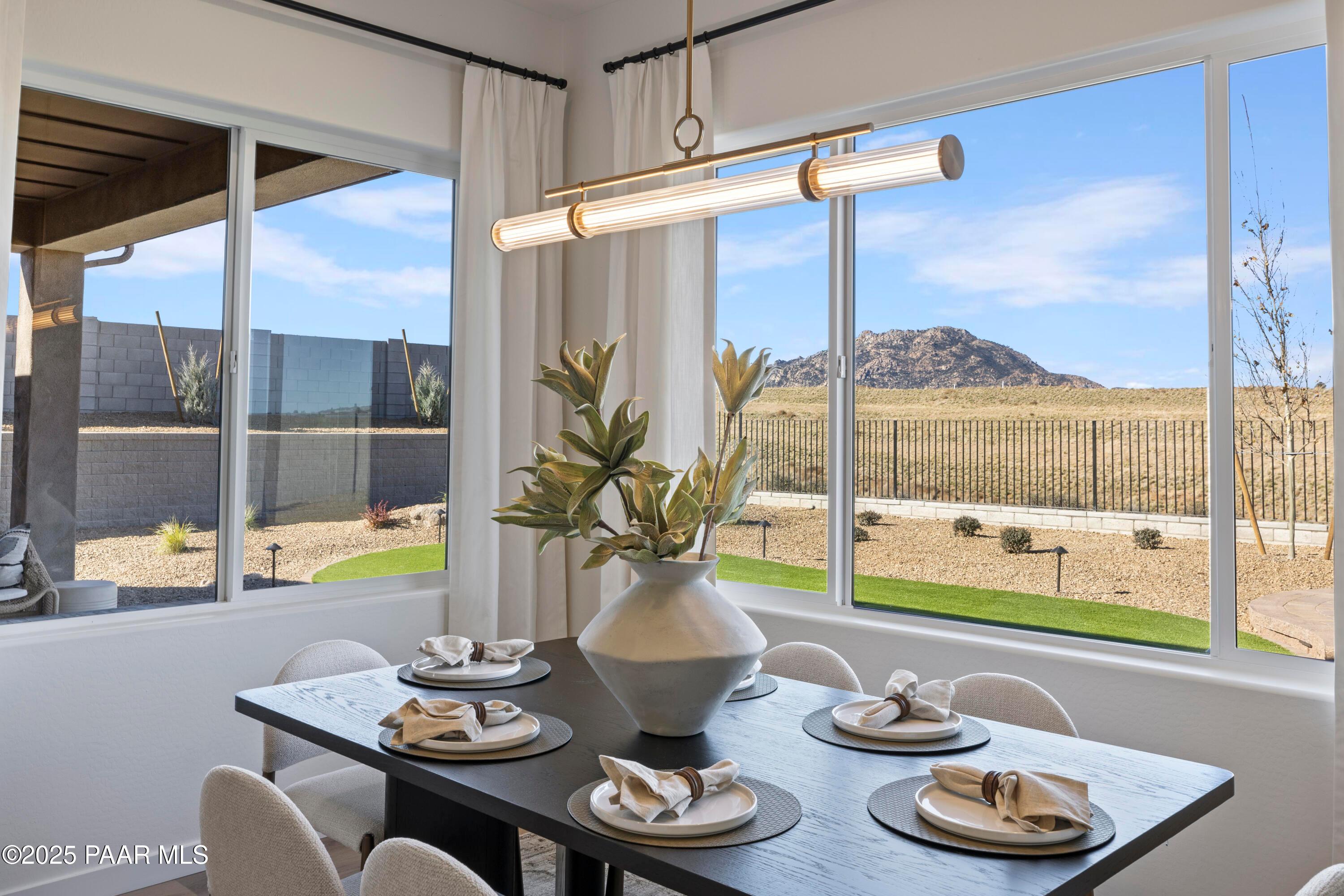 Modern dining area with set table, large potted plant, and desert mountain views through windows in Prescott, AZ home