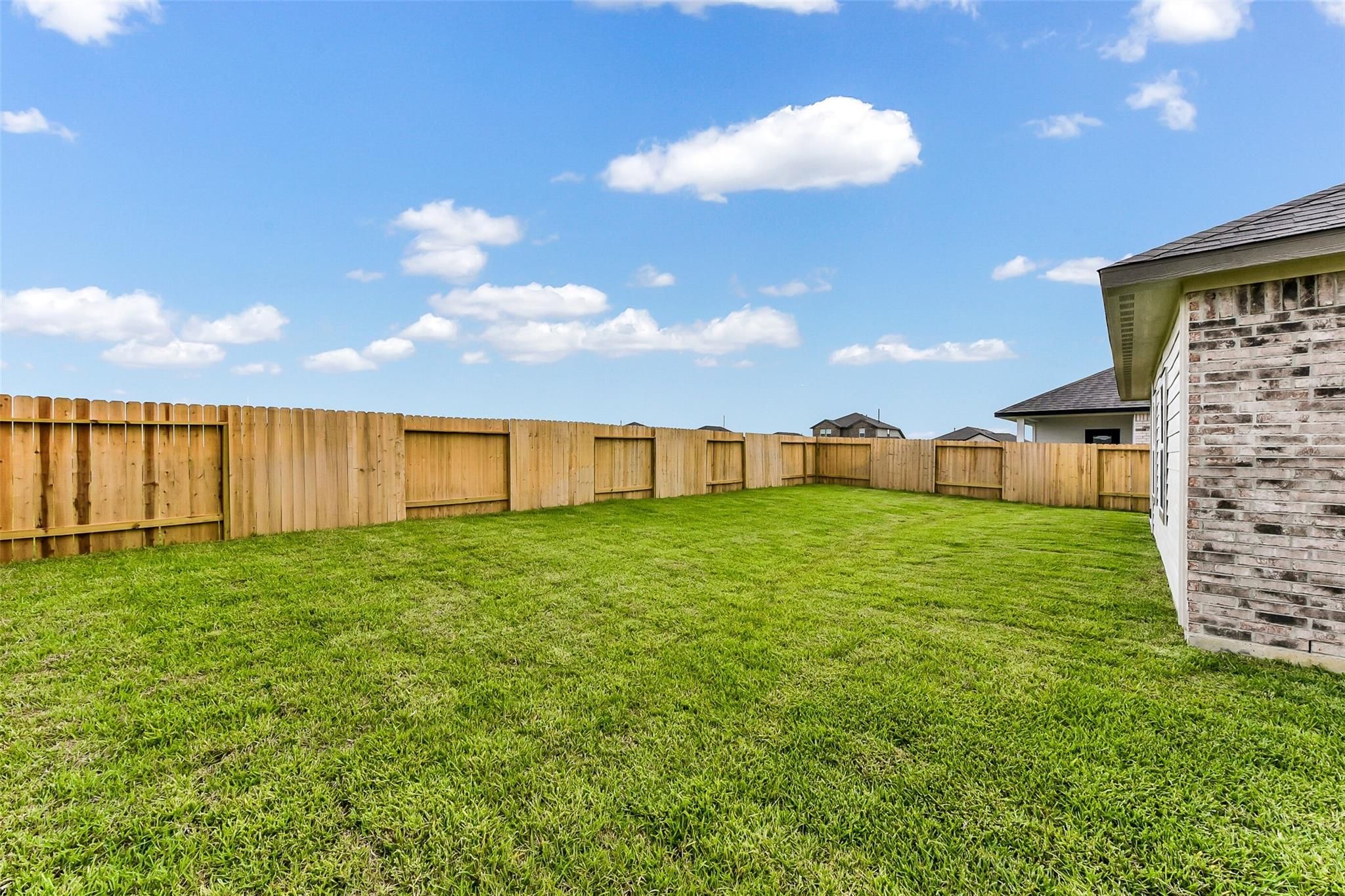 Private fenced backyard with lush green lawn and brick home exterior in Davidson Homes The Costa B, River Ranch Meadows, Dayton, Texas