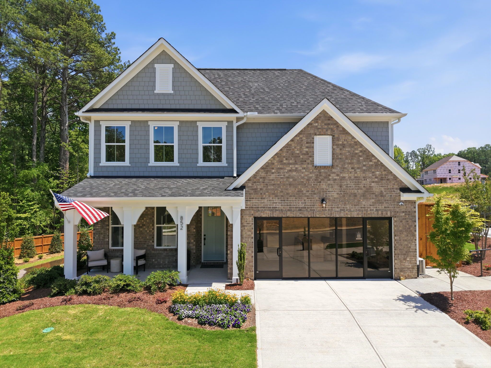 Contemporary gray siding home exterior at Sage on North Main in Wake Forest NC with covered porch, brick accents, and American flag by Davidson Homes