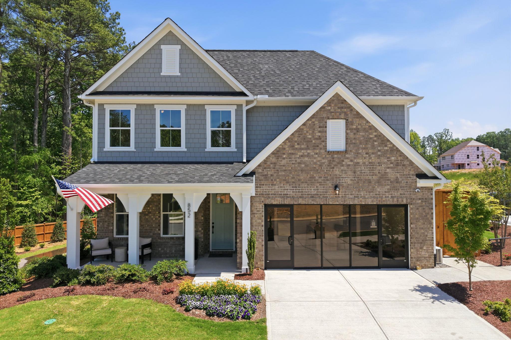 Contemporary gray siding home exterior at Sage on North Main in Wake Forest NC with covered porch, brick accents, and American flag by Davidson Homes