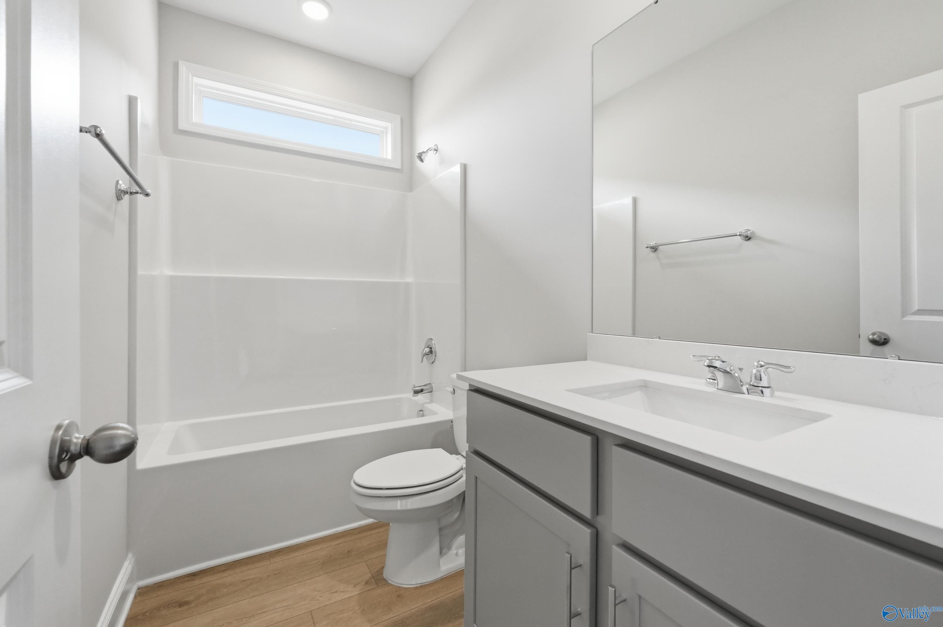 Bright secondary bathroom with white tub, shower, gray vanity, and mirror in Davidson Homes The Franklin, Meridianville, Alabama