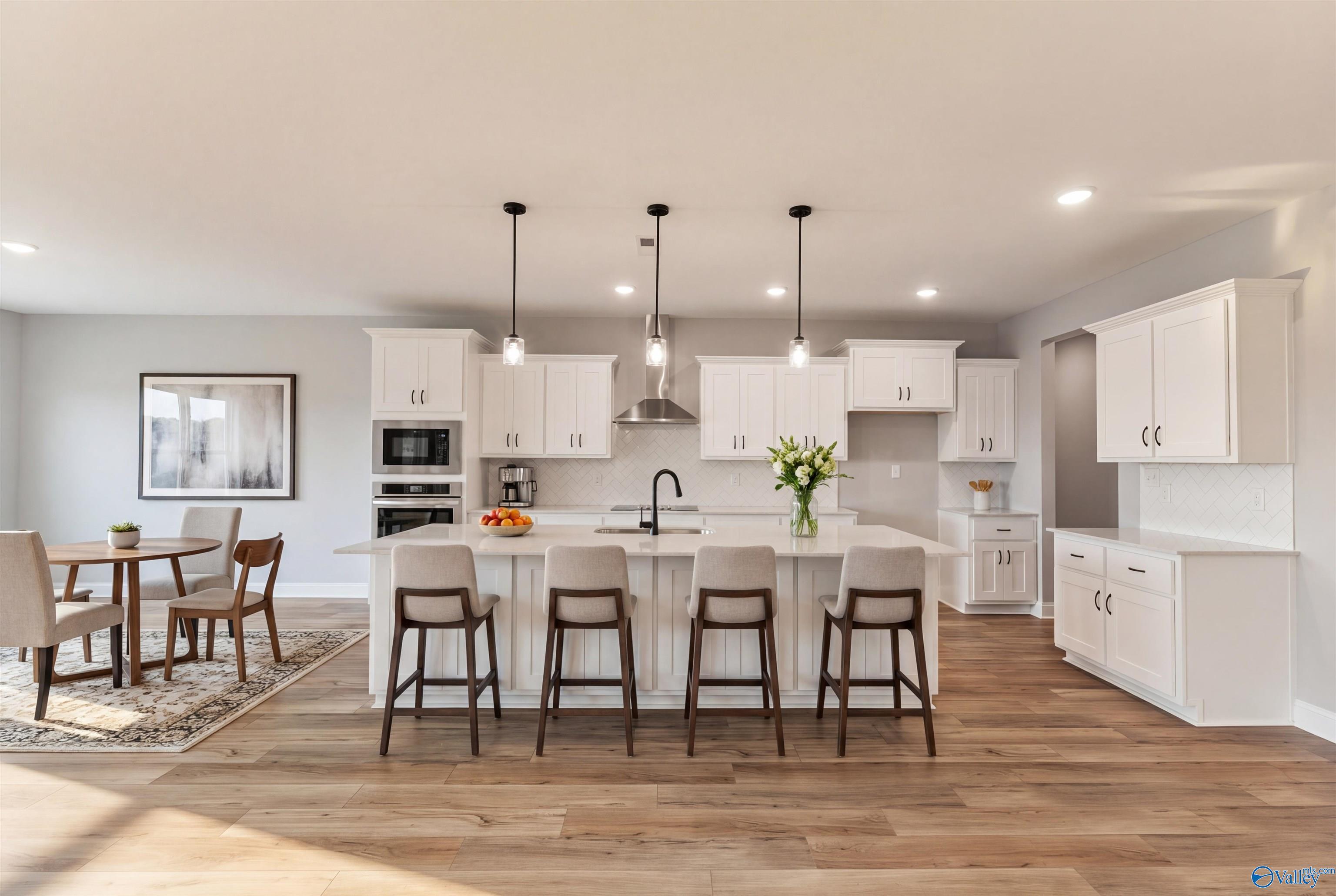 Modern open-concept kitchen with white island, stainless appliances, pendant lights, and dining area in The Finleigh home, Toney, Alabama