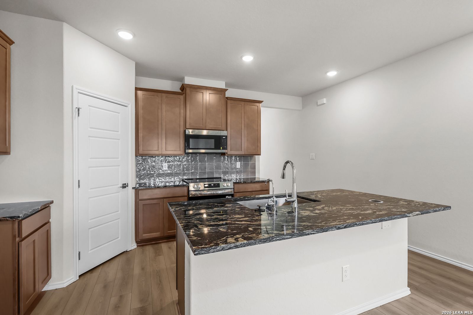 Modern kitchen with granite island and wood cabinets in San Marcos F floor plan at Rayburn Valley, San Antonio, Texas.