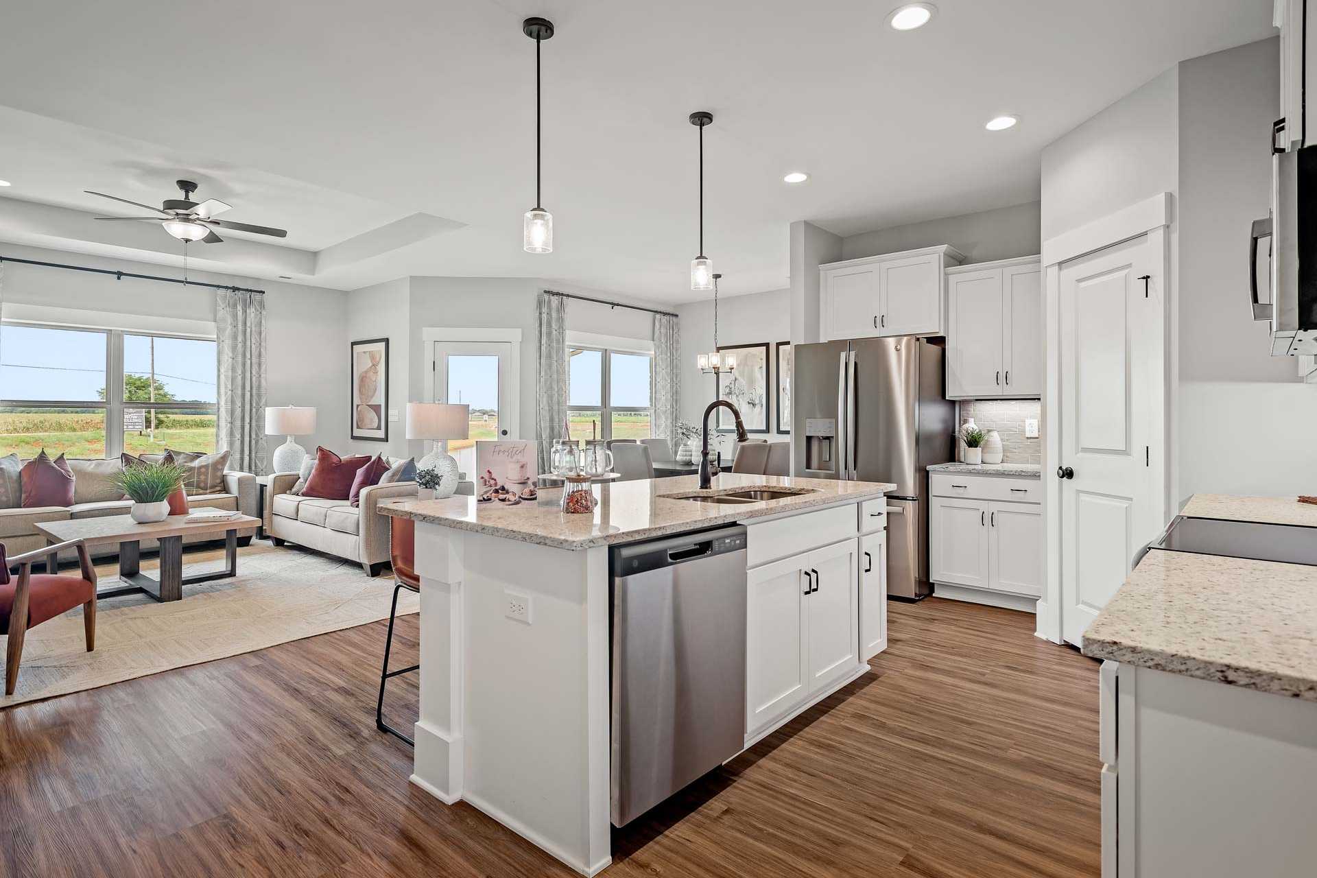 Open-concept kitchen and living room at Heritage Lakes in New Market Alabama with white cabinets, quartz island, hardwood floors