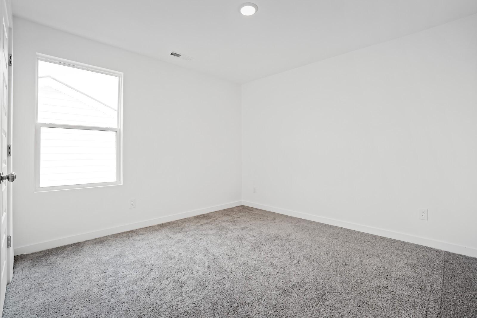 Bright bedroom with plush carpet and large window in The Logan B floor plan at Calista Farms, White House, Tennessee.