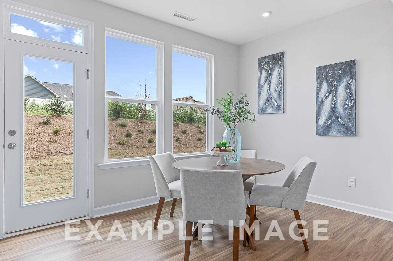 Bright breakfast nook in The Willow C home with round wood table, gray upholstered chairs, abstract blue art, and large windows to neighborhood