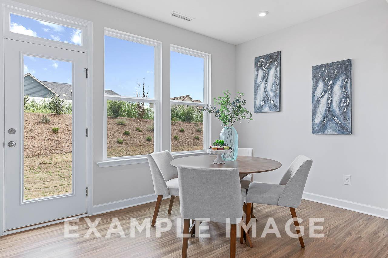 Bright breakfast nook in The Willow C home with round wood table, gray upholstered chairs, abstract blue art, and large windows to neighborhood