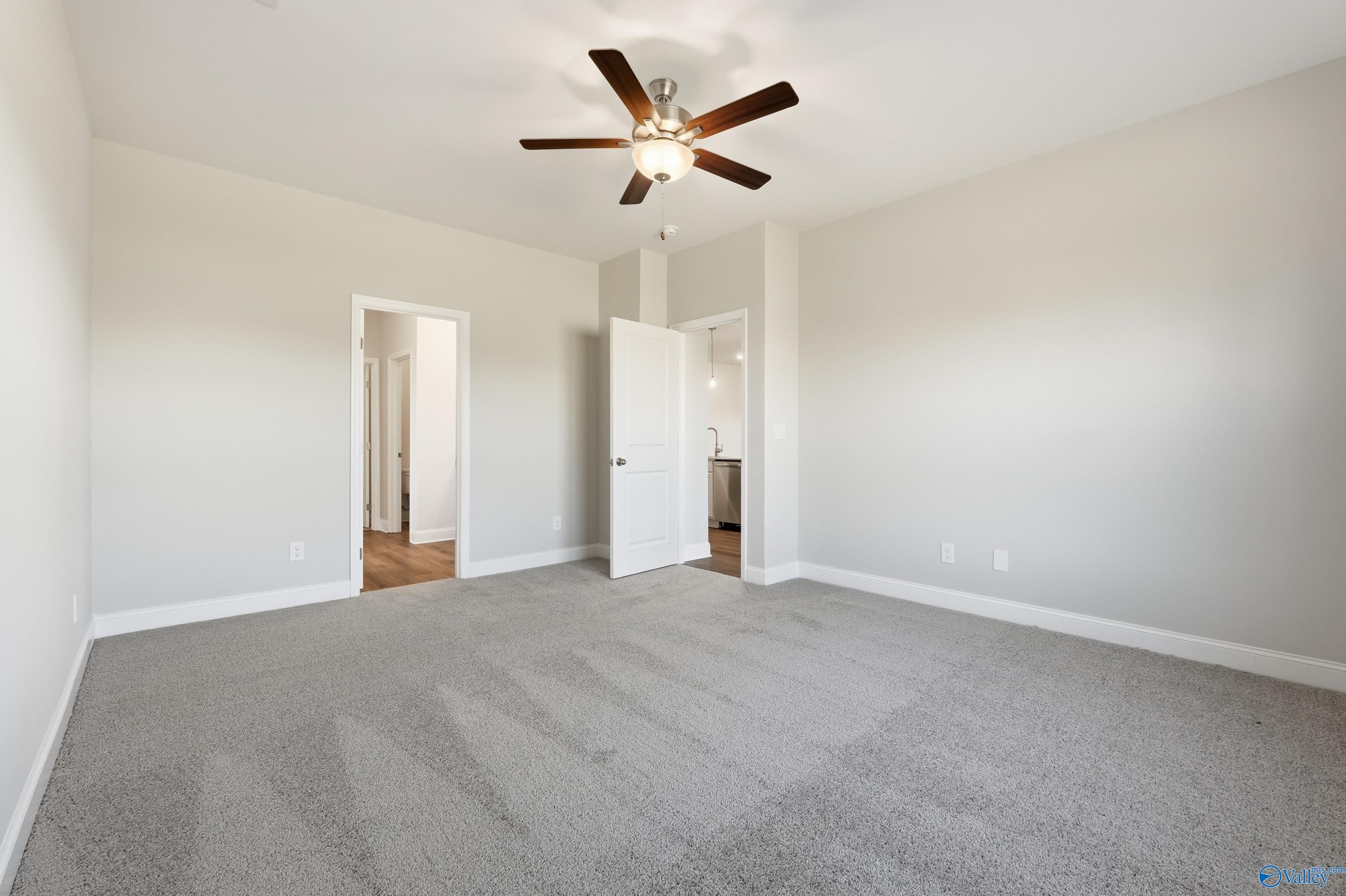 Spacious bedroom with ceiling fan, beige walls, gray carpet, and doors to bathroom and closet in Davidson Homes The Everett, Harvest, AL