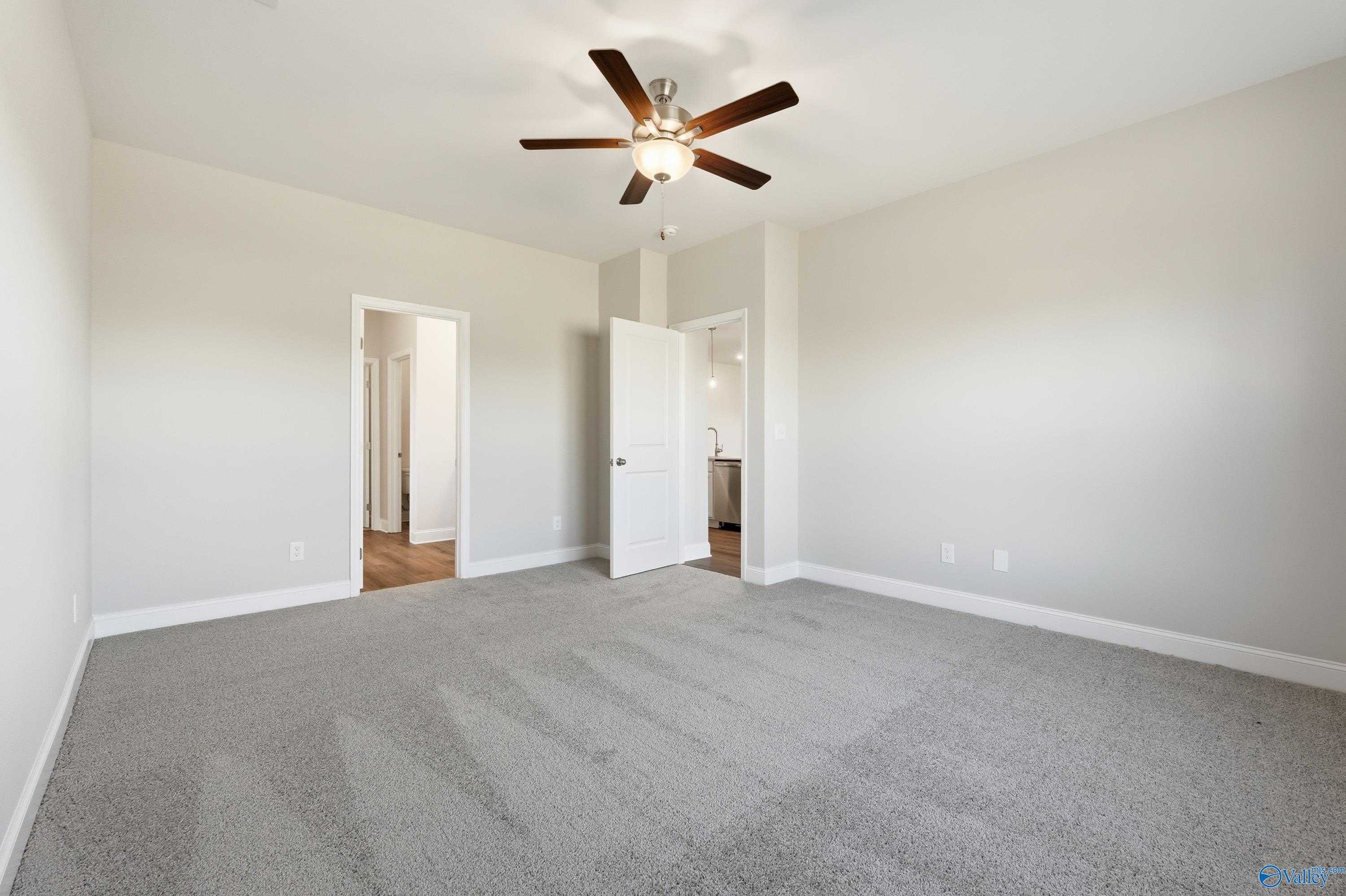 Spacious bedroom with ceiling fan, beige walls, gray carpet, and doors to bathroom and closet in Davidson Homes The Everett, Harvest, AL