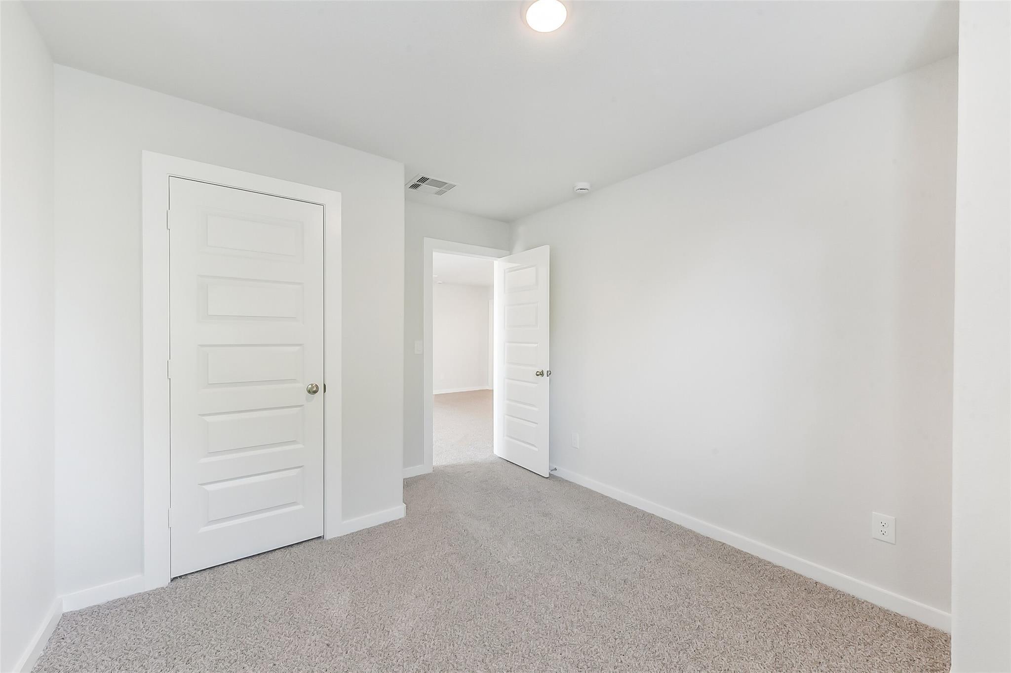 Bright secondary bedroom with white walls, carpet floor, and adjacent door in Davidson Homes Brazos E, Magnolia TX