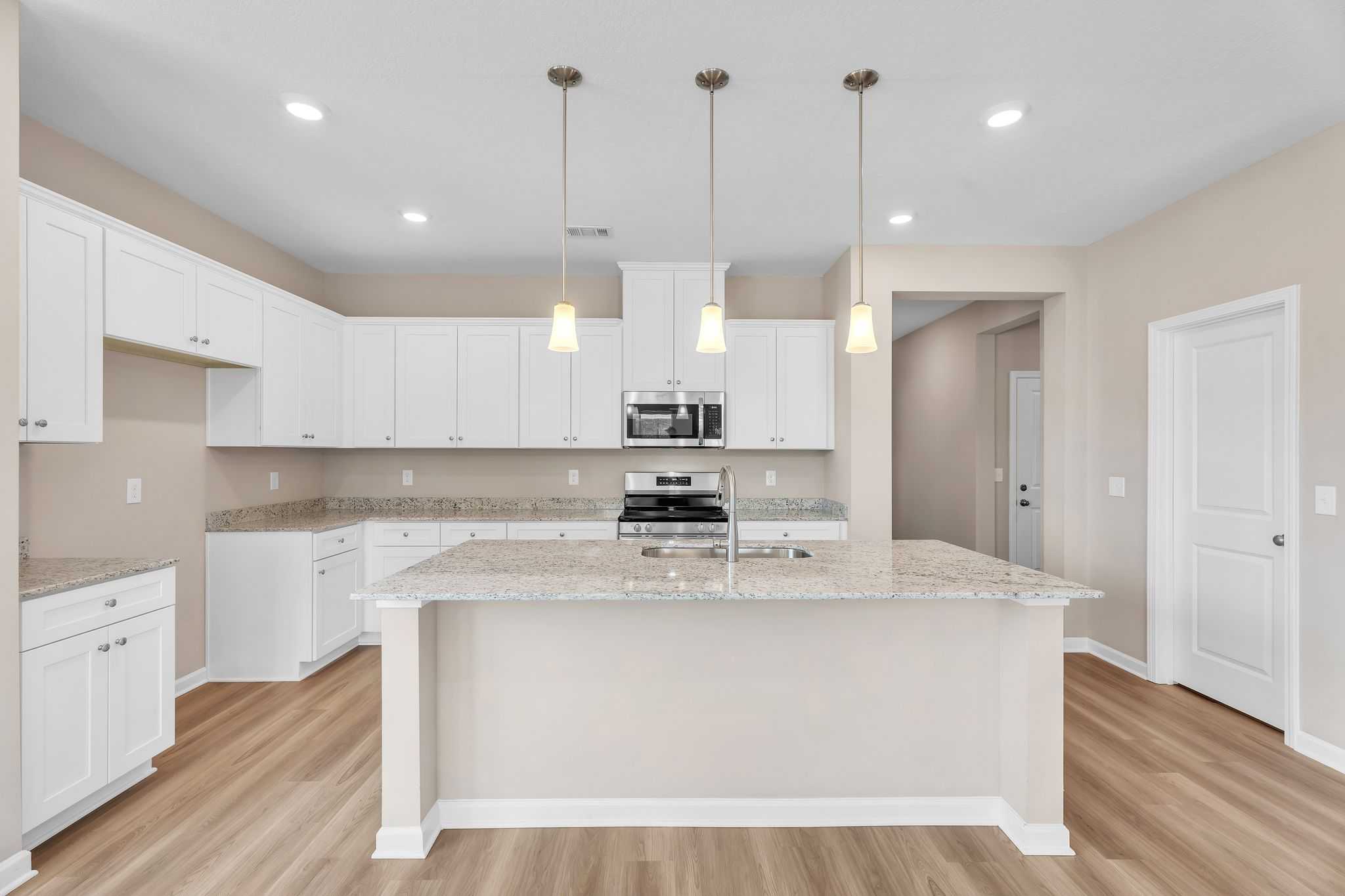 Spacious modern kitchen at Anderson Lakes in Opelika AL with white shaker cabinets granite island stainless appliances hardwood floors