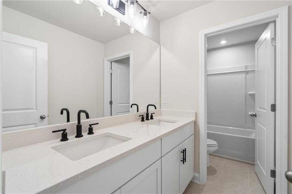 Modern double vanity bathroom with white quartz counters, black faucets, and adjacent shower in Davidson Homes The Hickory B, Buford GA