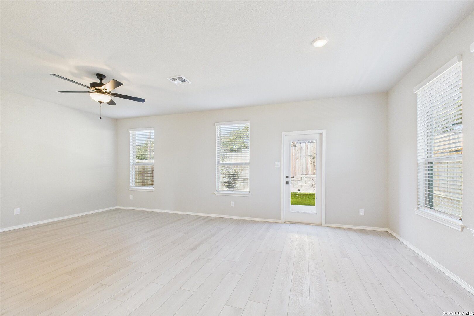 Bright living room with ceiling fan, large windows, blinds, and sliding door to lush backyard in Davidson Homes The Charlotte A, San Antonio