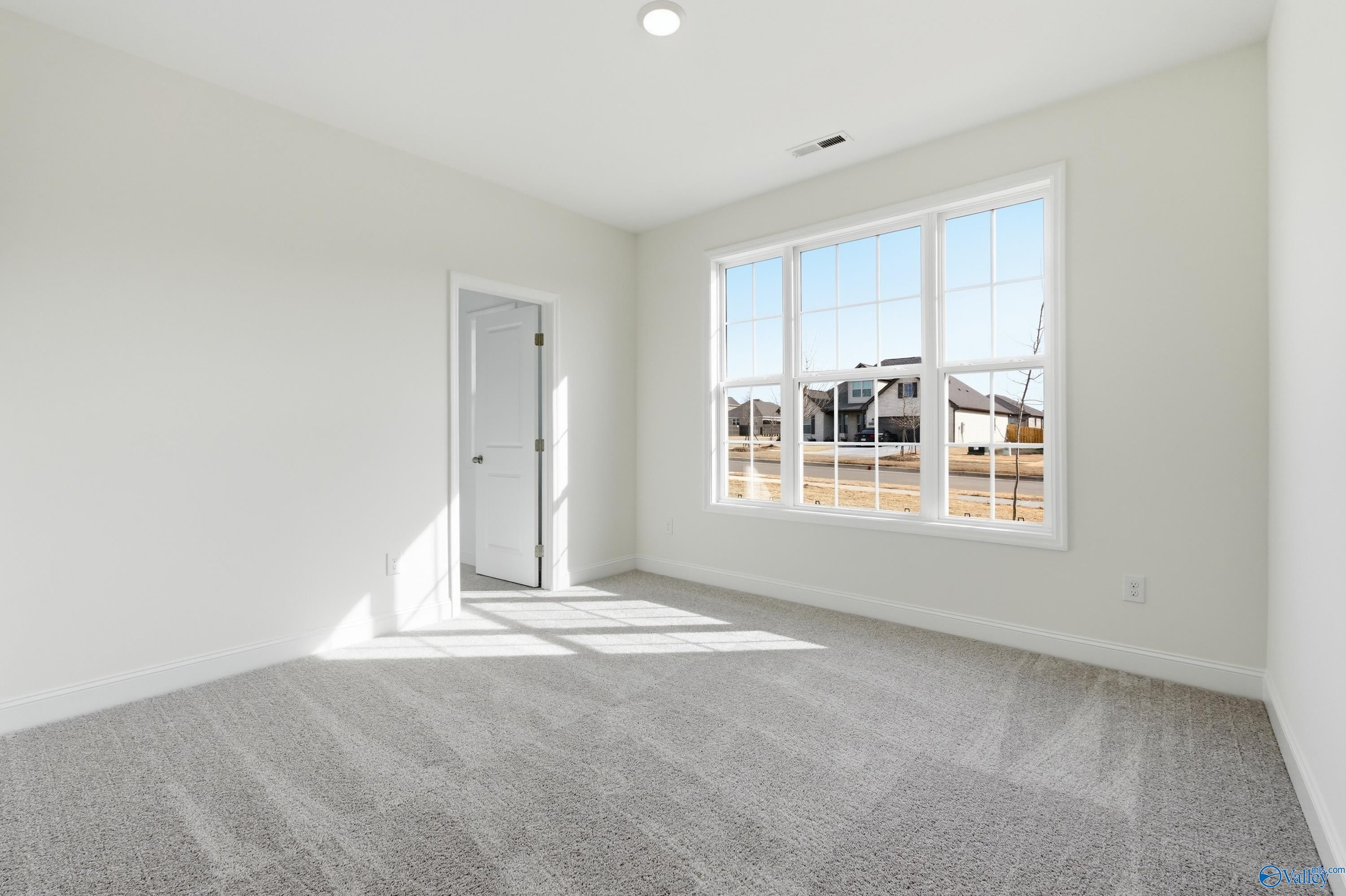 Bright secondary bedroom with white walls, gray carpet, and large sunny windows in Davidson Homes The Montgomery C, Harvest, Alabama