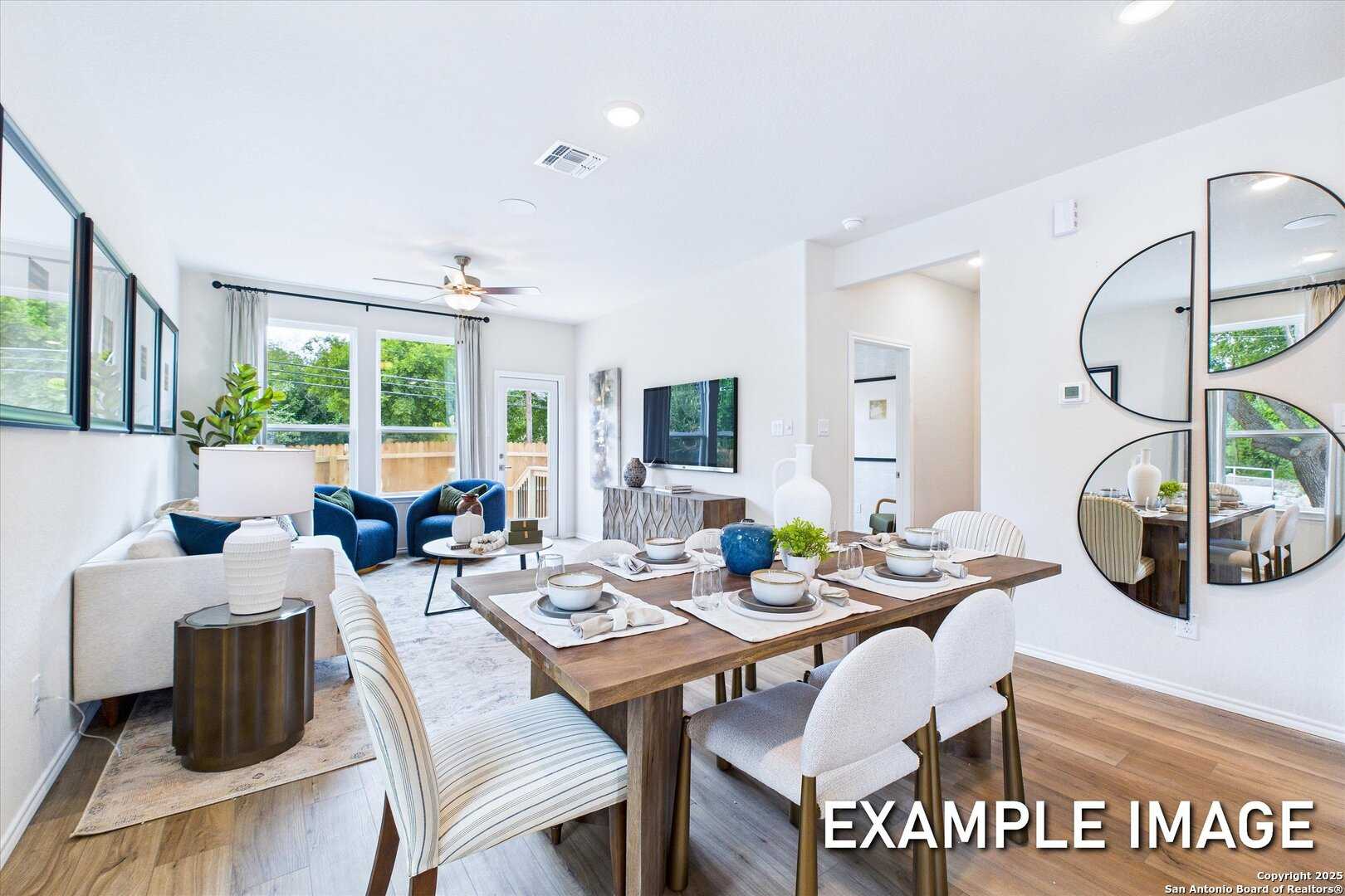 Modern dining area with wooden table set for meal, white chairs, open to living room with TV and French doors in Davidson Homes The Gillian C, San Antonio