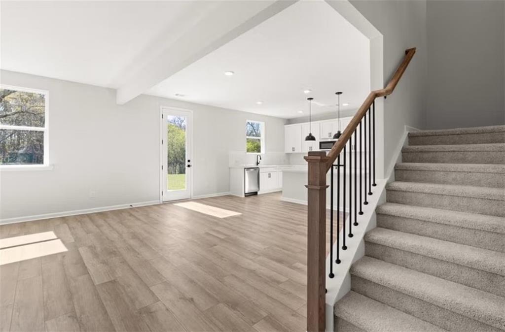 Open-concept living and kitchen with white cabinets, stainless appliances, hardwood floors, and carpeted staircase in Davidson Homes Hickory B, Winder GA