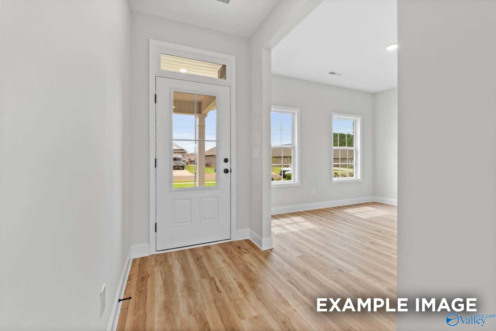 Bright entry foyer with white glass-paneled door, hardwood floors, and large windows in Davidson Homes Shelby A, Athens Alabama