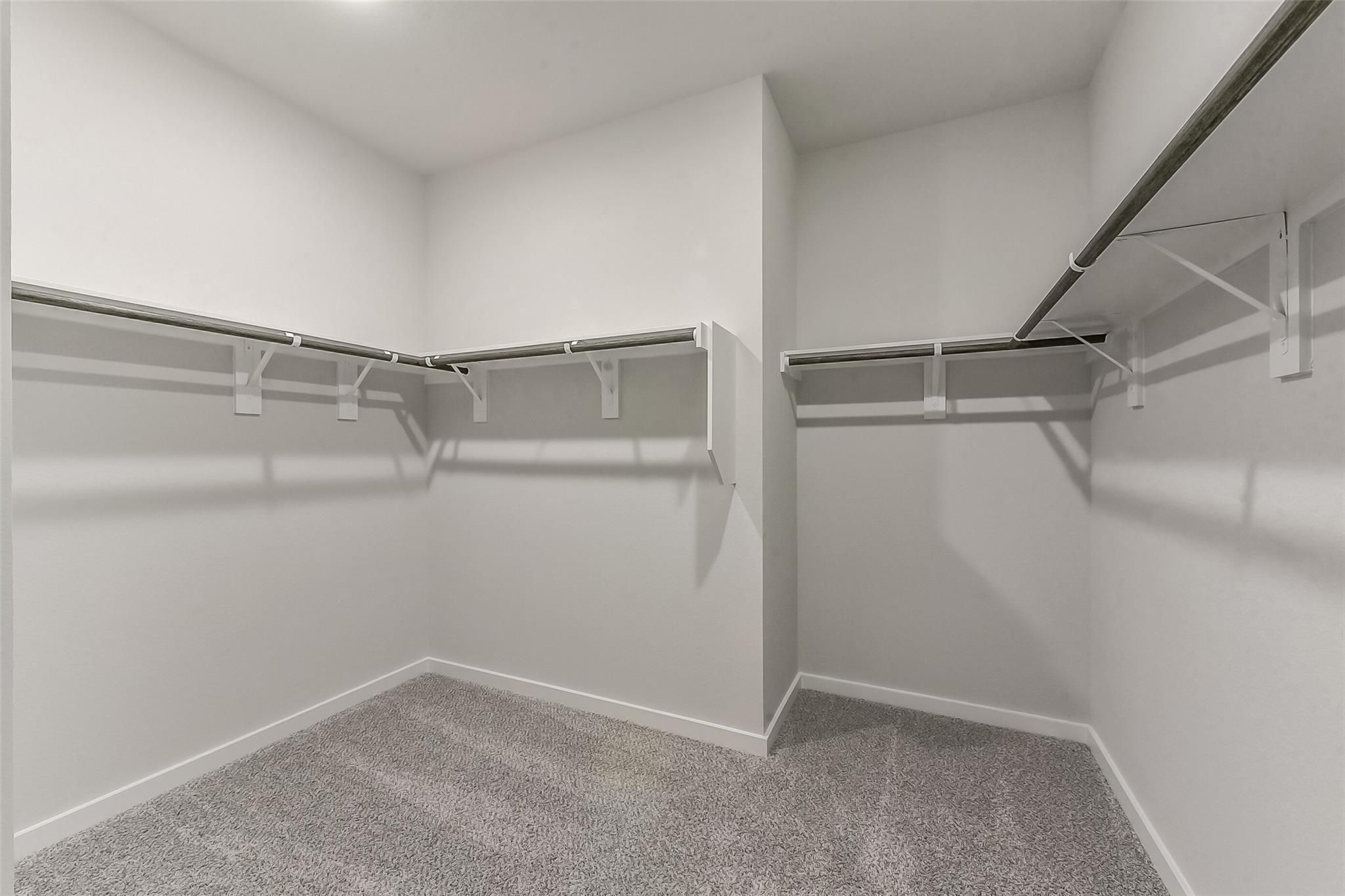 Spacious L-shaped walk-in closet with gray carpet, white walls, and built-in hanging rods in Davidson Homes The Everett C, Crosby, Texas
