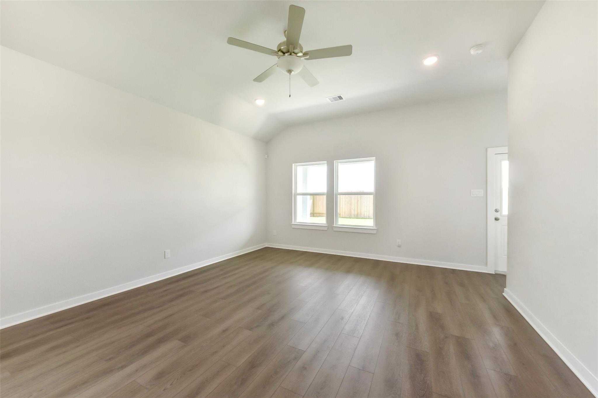Spacious empty bedroom with hardwood floors, ceiling fan, and large windows in Davidson Homes The Laguna C, Dayton, Texas