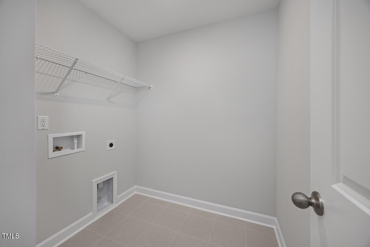 Functional laundry room with wire shelving, washer-dryer hookups and tiled floor in Davidson Homes The Warren plan, Fuquay-Varina, NC
