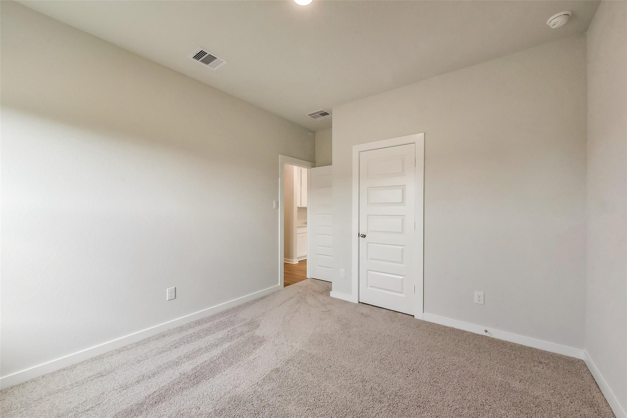 Spacious secondary bedroom with beige carpet, light walls, and open bathroom door in Davidson Homes The Frio G, Dayton, Texas