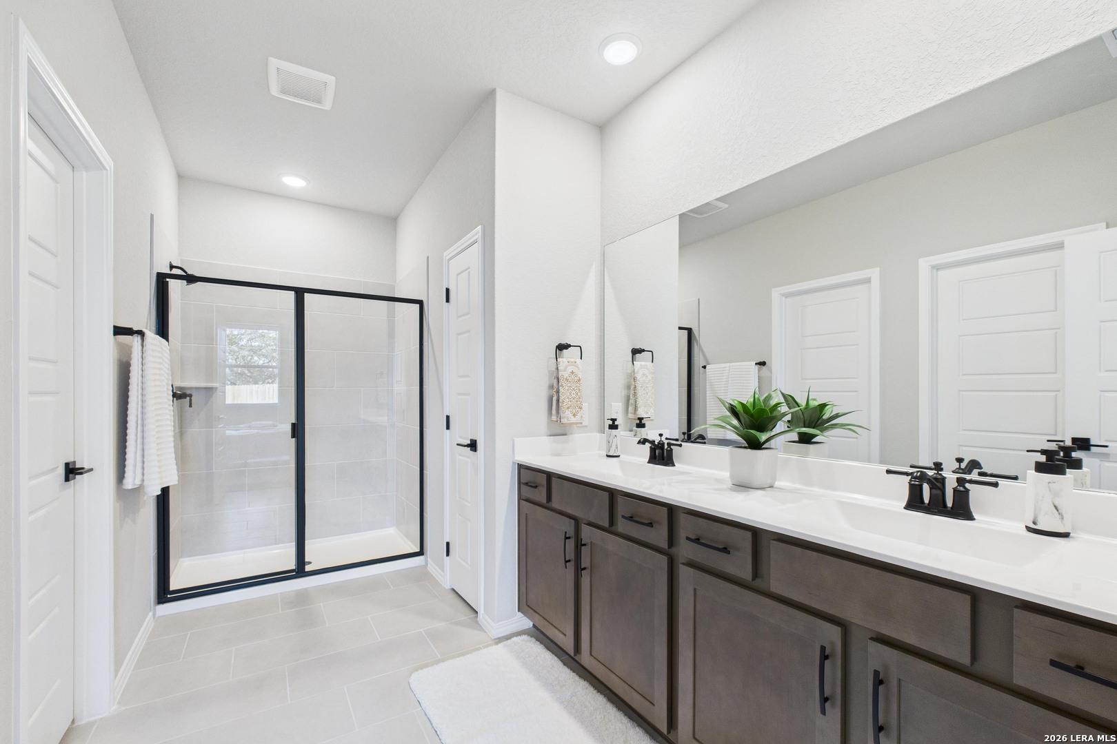 Modern master bathroom with dark wood double vanity, black-framed glass shower, and white tile in Davidson Homes The Douglas E, Bricewood, San Antonio