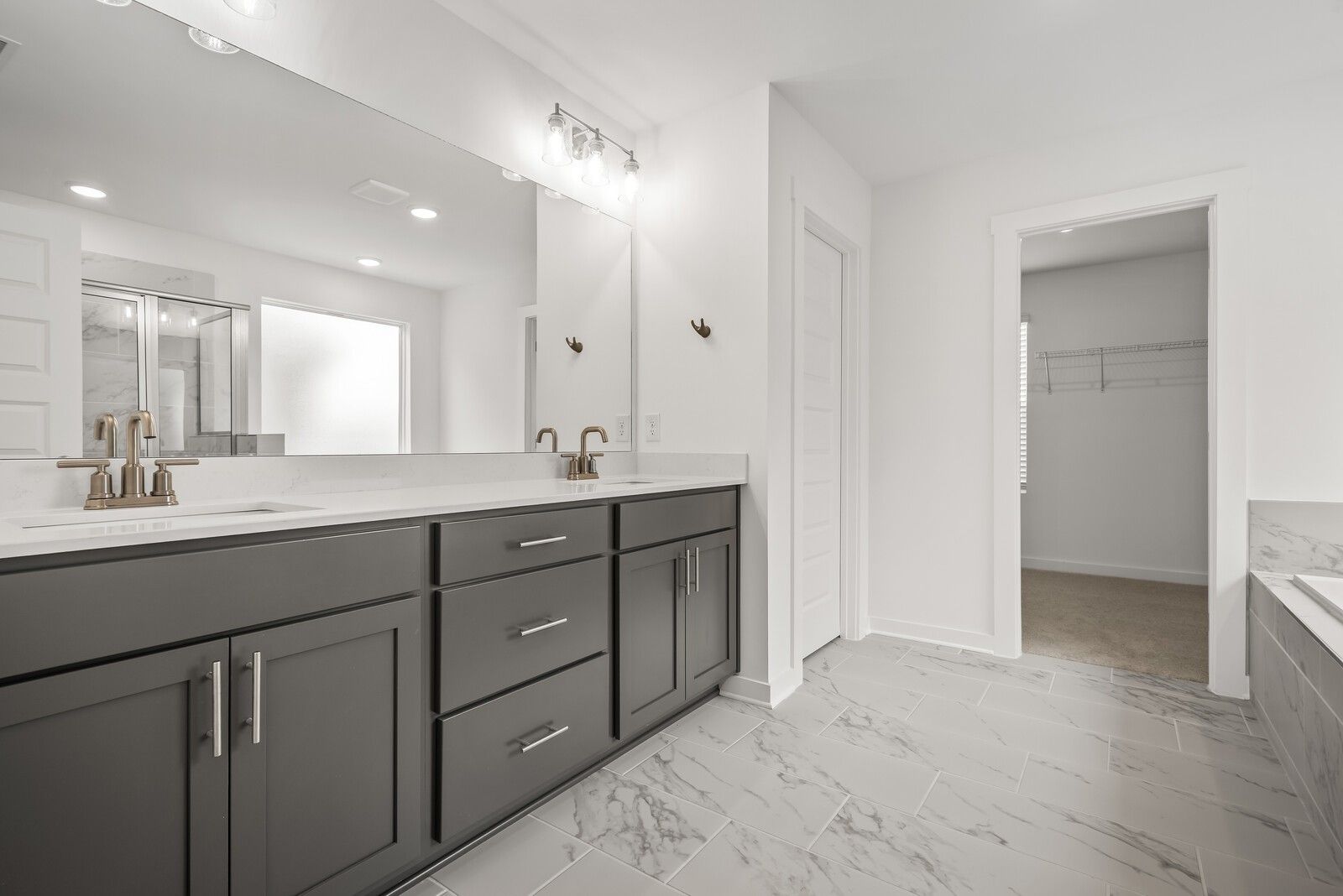 Spacious master bathroom with double gray vanity, white quartz counters, large mirror, and marble tile floor in Davidson Homes The Gordon C, White House, TN