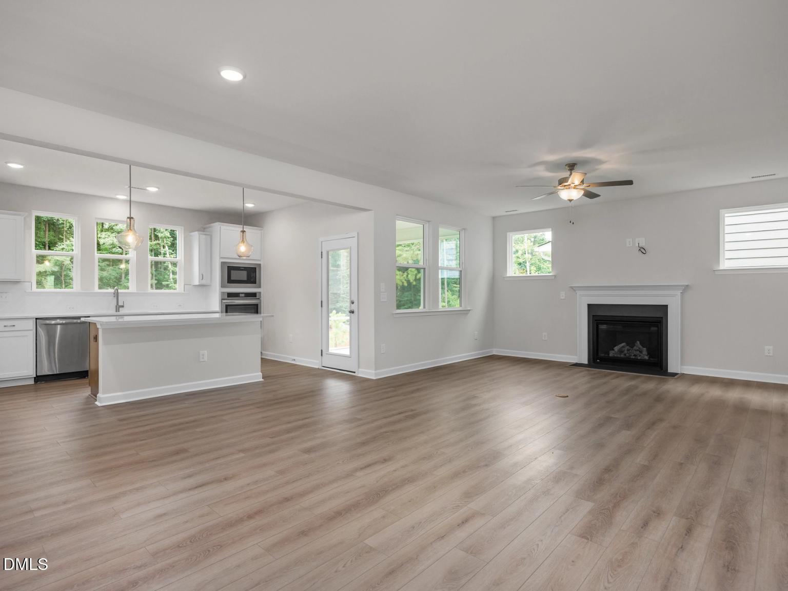 Open kitchen with white island, stainless appliances, and adjacent living room featuring gas fireplace and hardwood floors in Davidson Homes The Aspen, Wake Forest