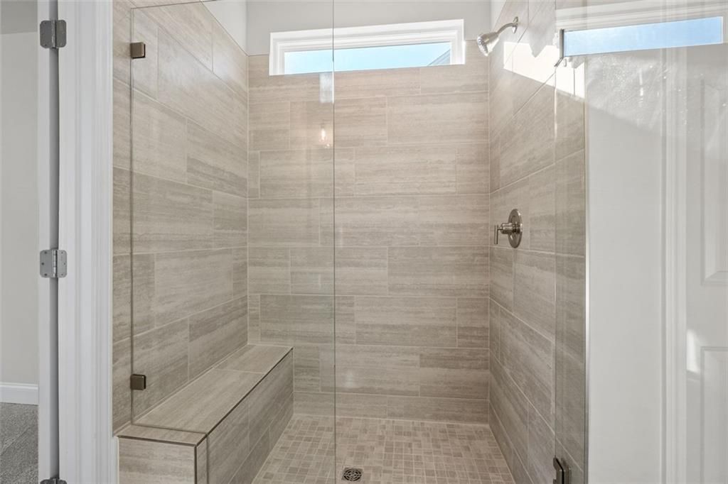 Luxurious walk-in shower with frameless glass enclosure, tiled bench, and clerestory windows in Davidson Homes The Ash C, Hoschton, GA