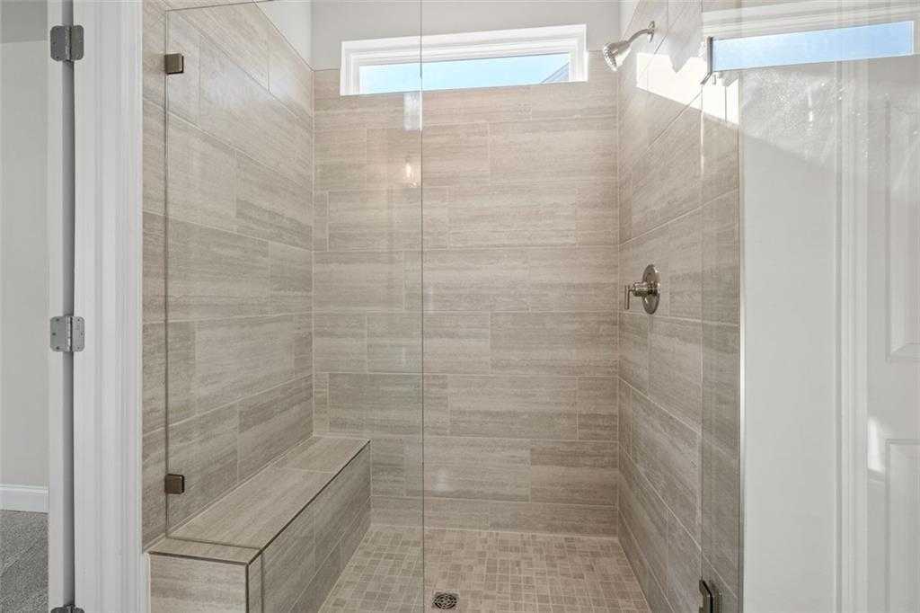 Luxurious walk-in shower with frameless glass enclosure, tiled bench, and clerestory windows in Davidson Homes The Ash C, Hoschton, GA