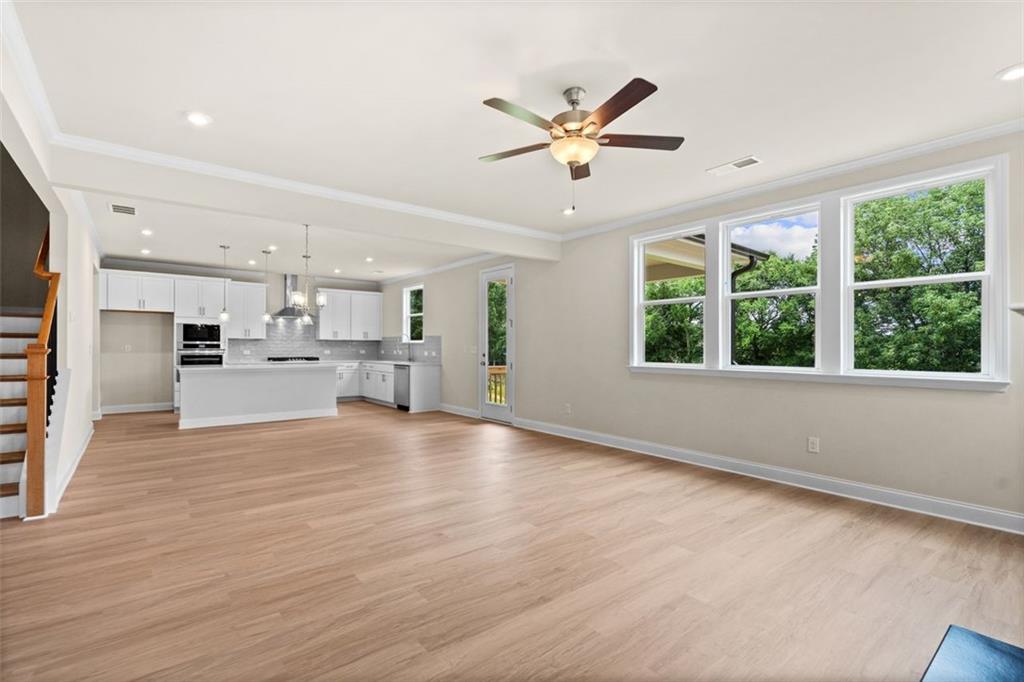 Spacious open kitchen-living area with white cabinets, island sink, hardwood floors, and large windows in The Hickory B home, Wehunt Meadows, Hoschton