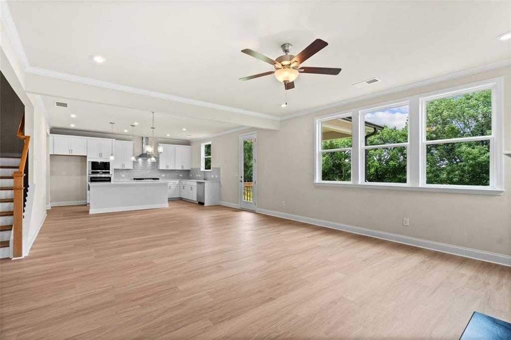 Spacious open kitchen-living area with white cabinets, island sink, hardwood floors, and large windows in The Hickory B home, Wehunt Meadows, Hoschton