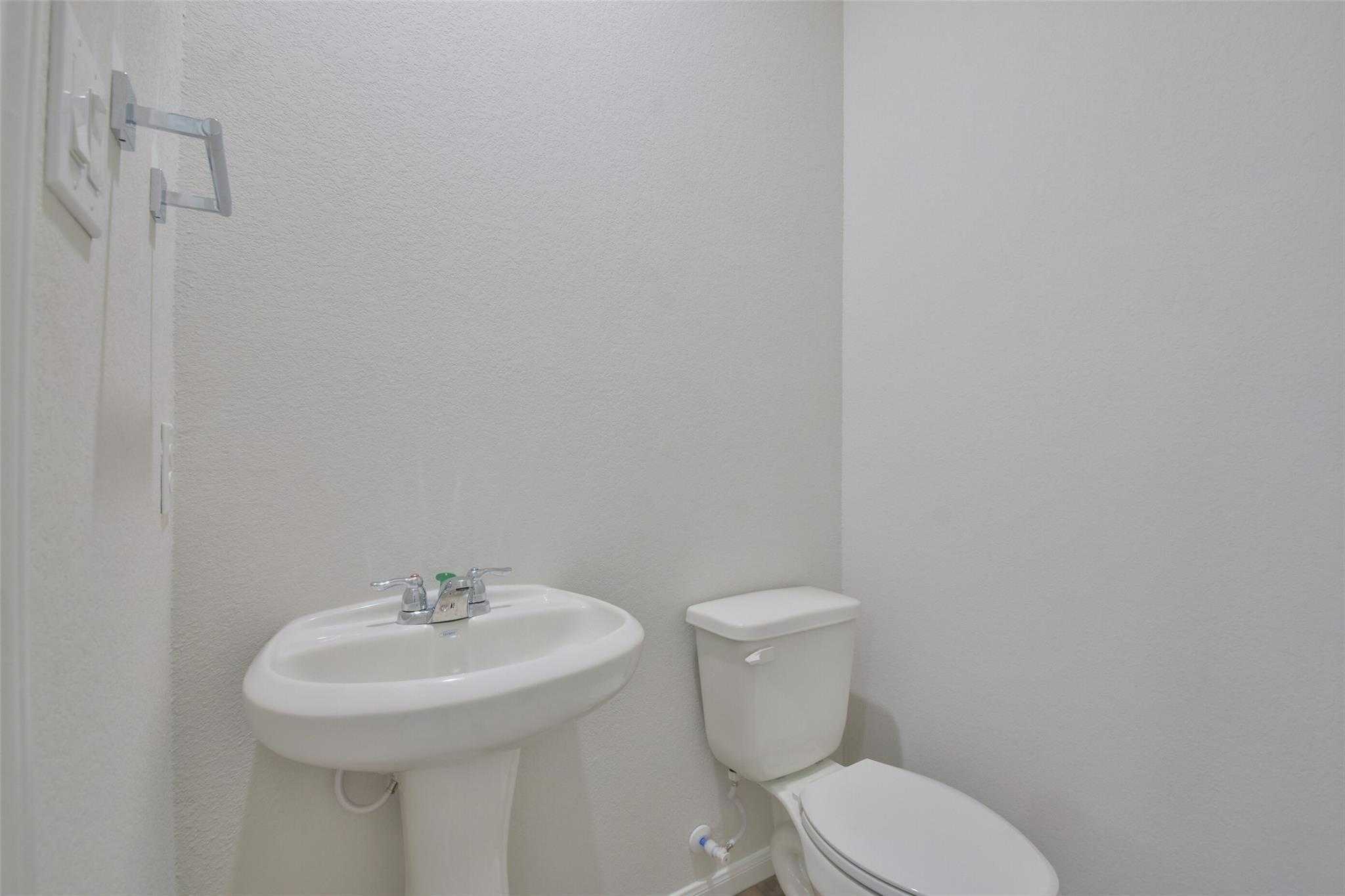 Clean white half bathroom featuring pedestal sink and toilet in Davidson Homes The Tierra A, Dayton, Texas