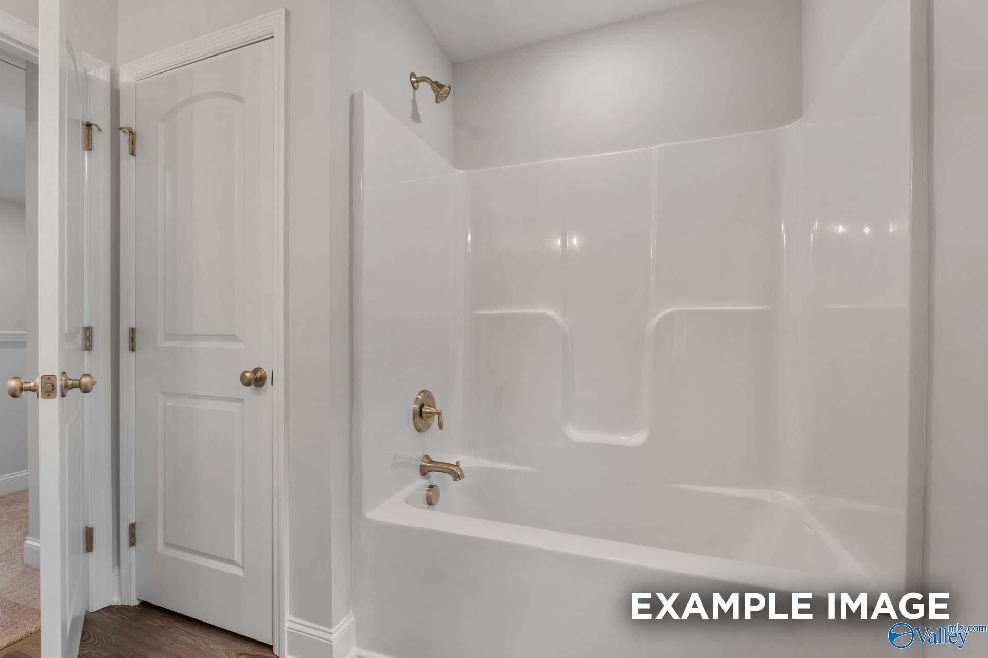 Bright bathroom with white tub-shower combo, brass fixtures, and neutral walls in The Shelby C by Davidson Homes, Arab, Alabama