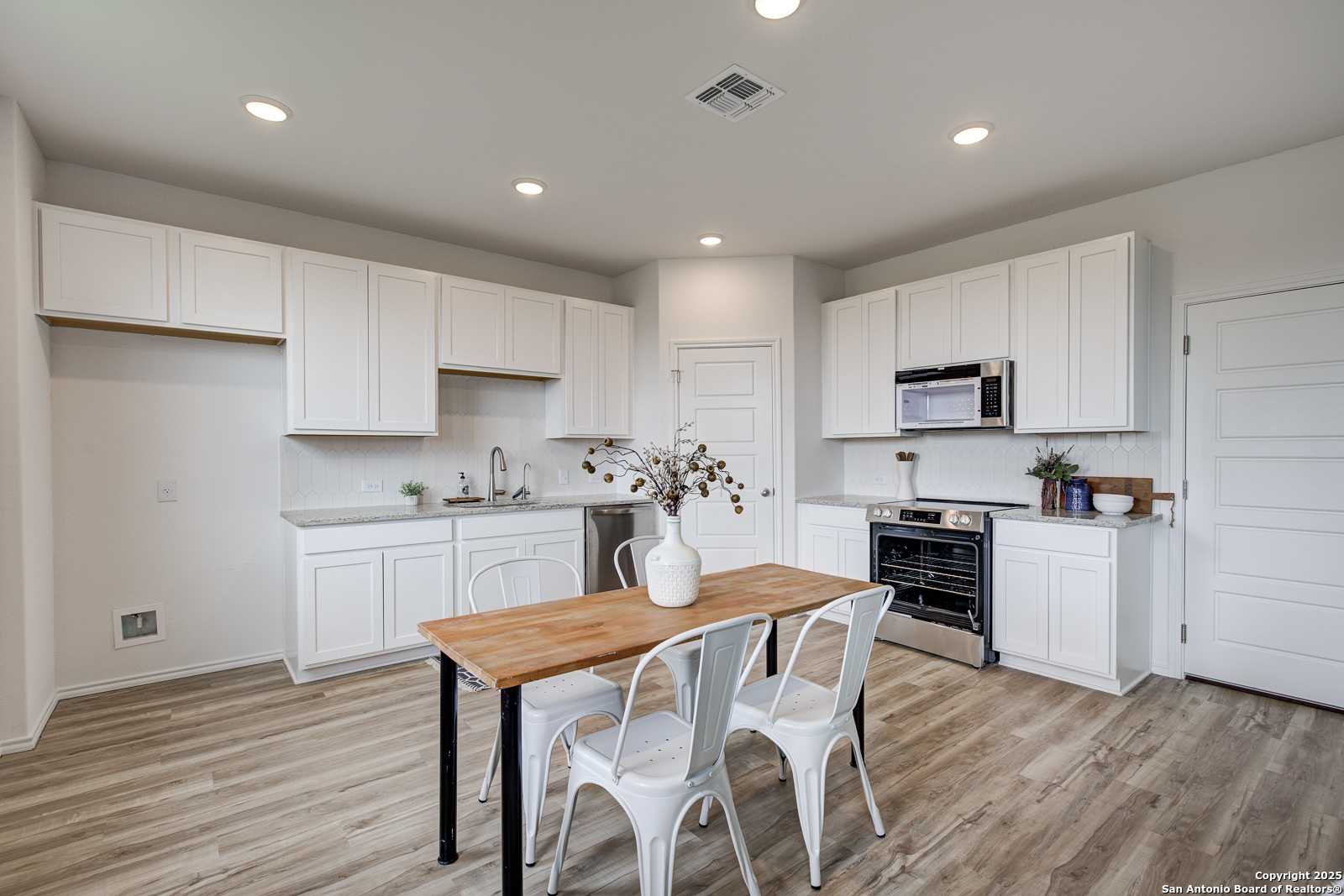 Bright kitchen with white shaker cabinets, stainless appliances, farmhouse sink, and wooden dining table in Davidson Homes The Trinity A, San Antonio