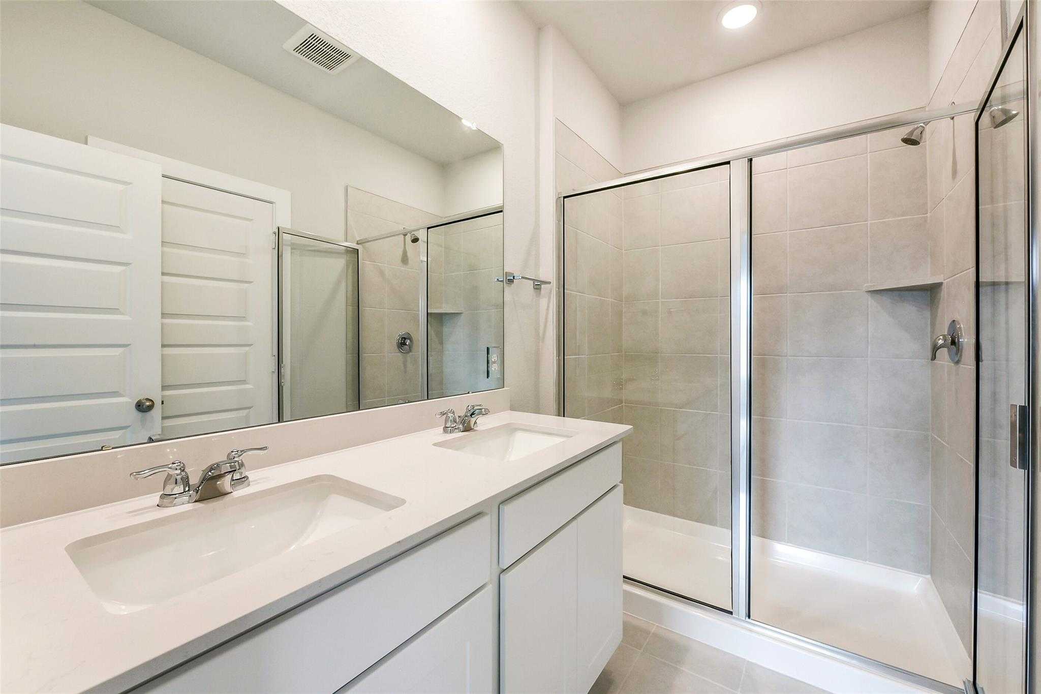 Modern master bathroom featuring double vanity, frameless glass shower, and neutral tile in Davidson Homes The Comal G, Dayton, Texas