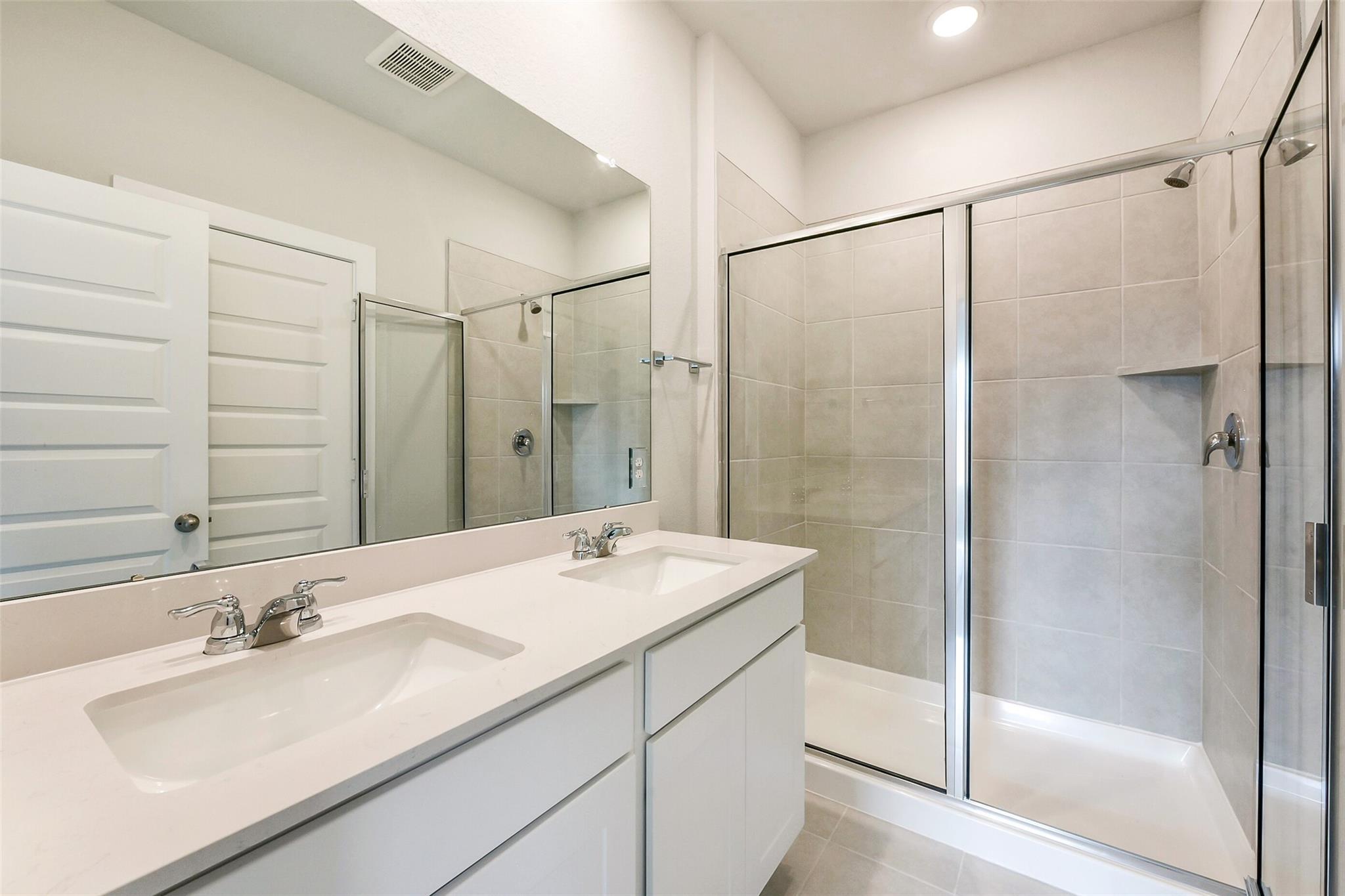 Modern master bathroom with double white vanity, frameless glass shower, and tile walls in Davidson Homes The Comal G, Dayton, Texas