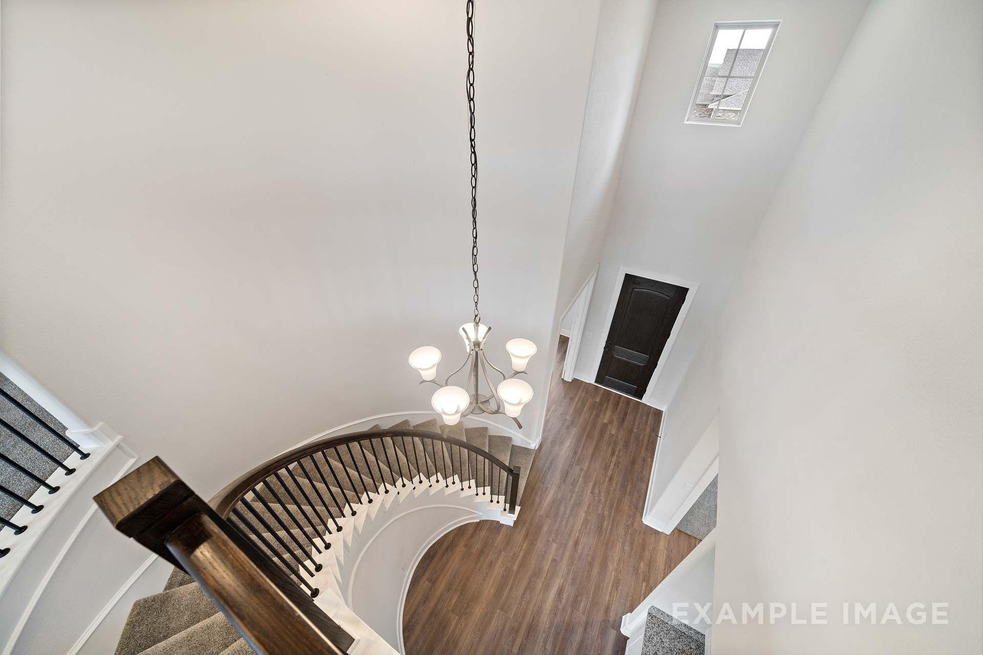Two-story curved staircase with wrought iron balusters and chandelier in The Victoria foyer, Davidson Homes Texas City.