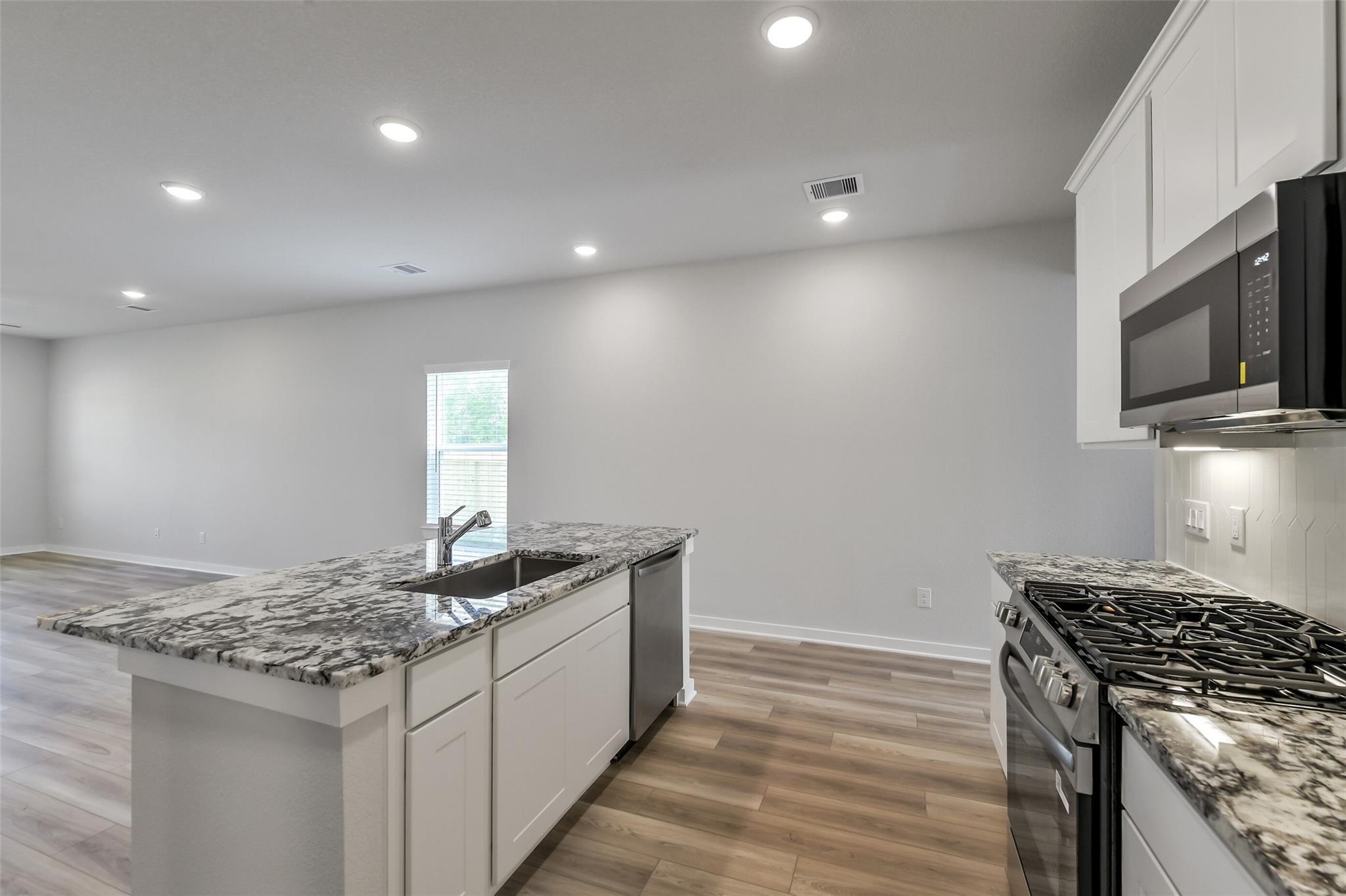Spacious kitchen with granite island, white cabinets, stainless gas range and microwave in San Marcos E home, Conroe Texas