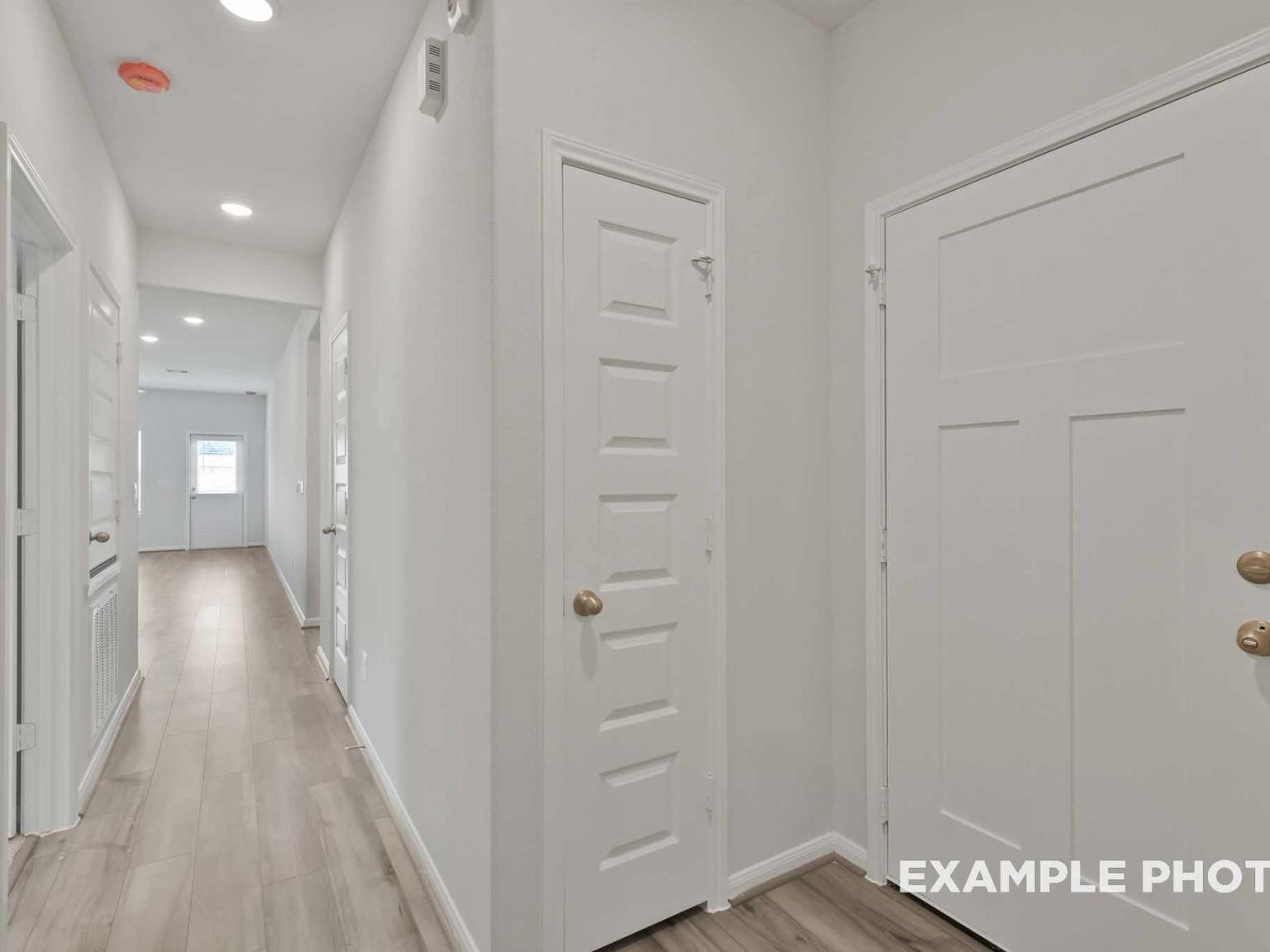 Bright hallway with white paneled walls, light oak floors, and recessed lighting in Davidson Homes The Comal F, Conroe, Texas