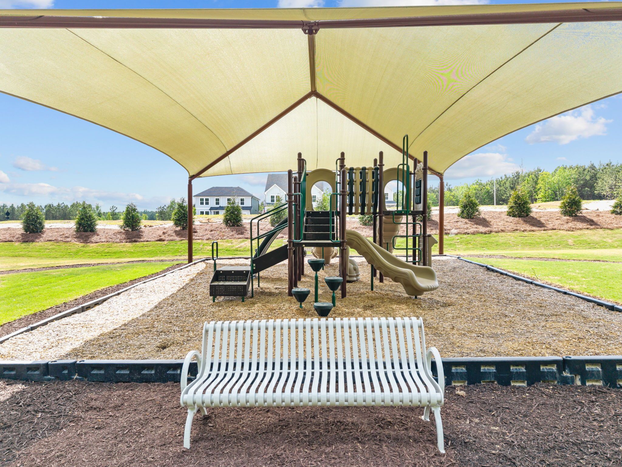 Shaded playground at Wendell Ridge in Wendell, NC with climbing structures, slides, and park bench seating.