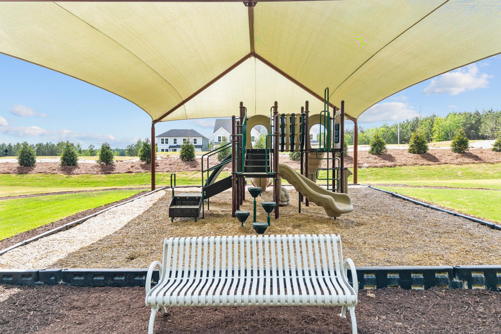 Shaded playground at Wendell Ridge in Wendell, NC with climbing structures, slides, and park bench seating.