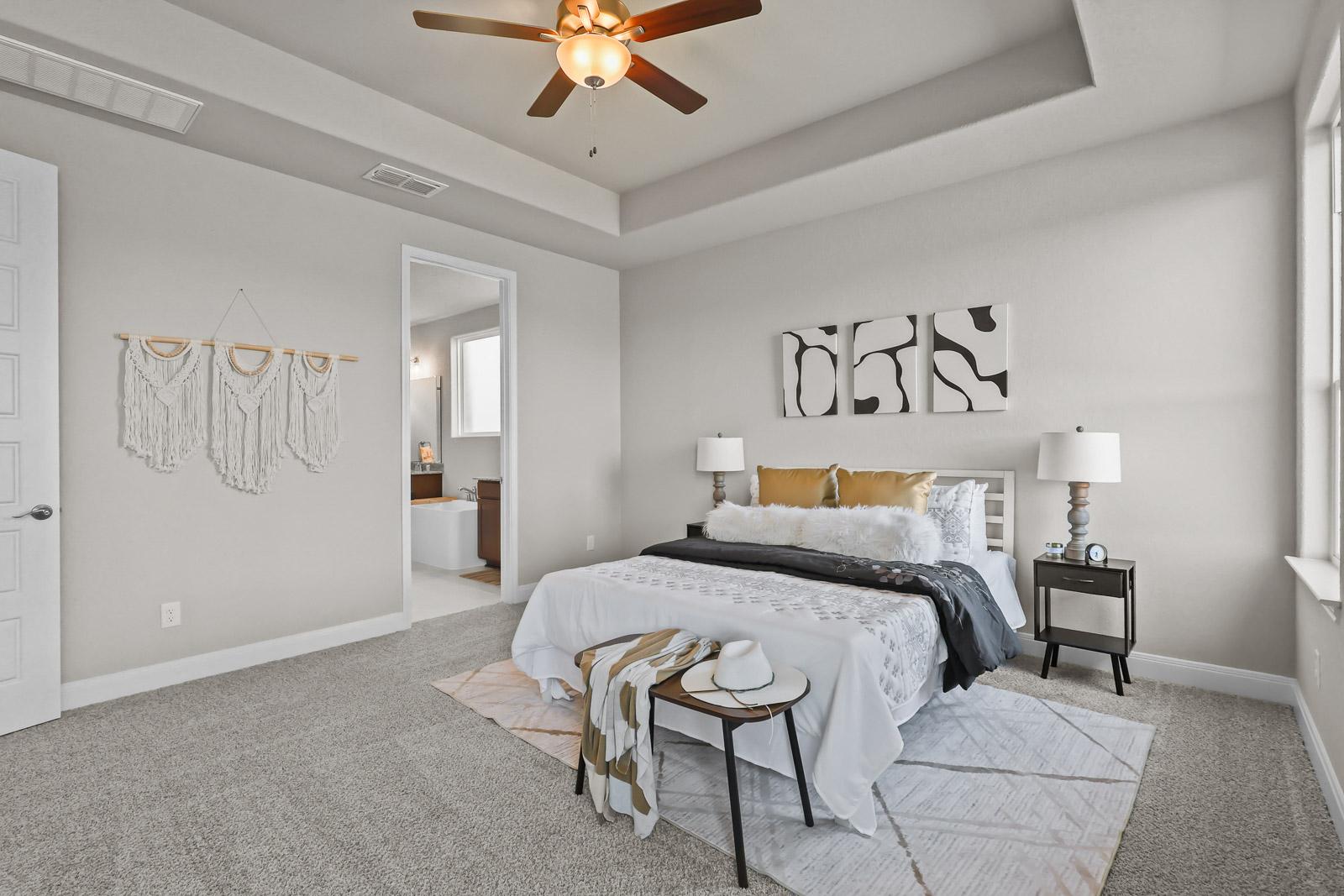 Spacious master suite on the main floor of The Jennings G featuring a tray ceiling, plush bedding, and an attached bath.