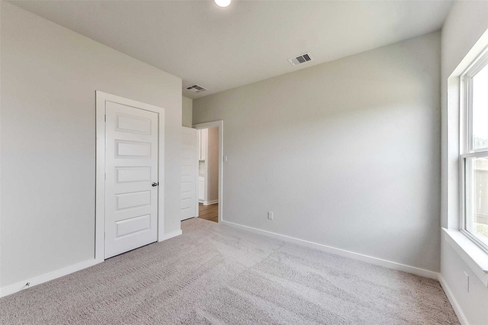 Light gray secondary bedroom with carpet flooring, paneled door, and adjacent bathroom in Davidson Homes The Frio F, Dayton, Texas