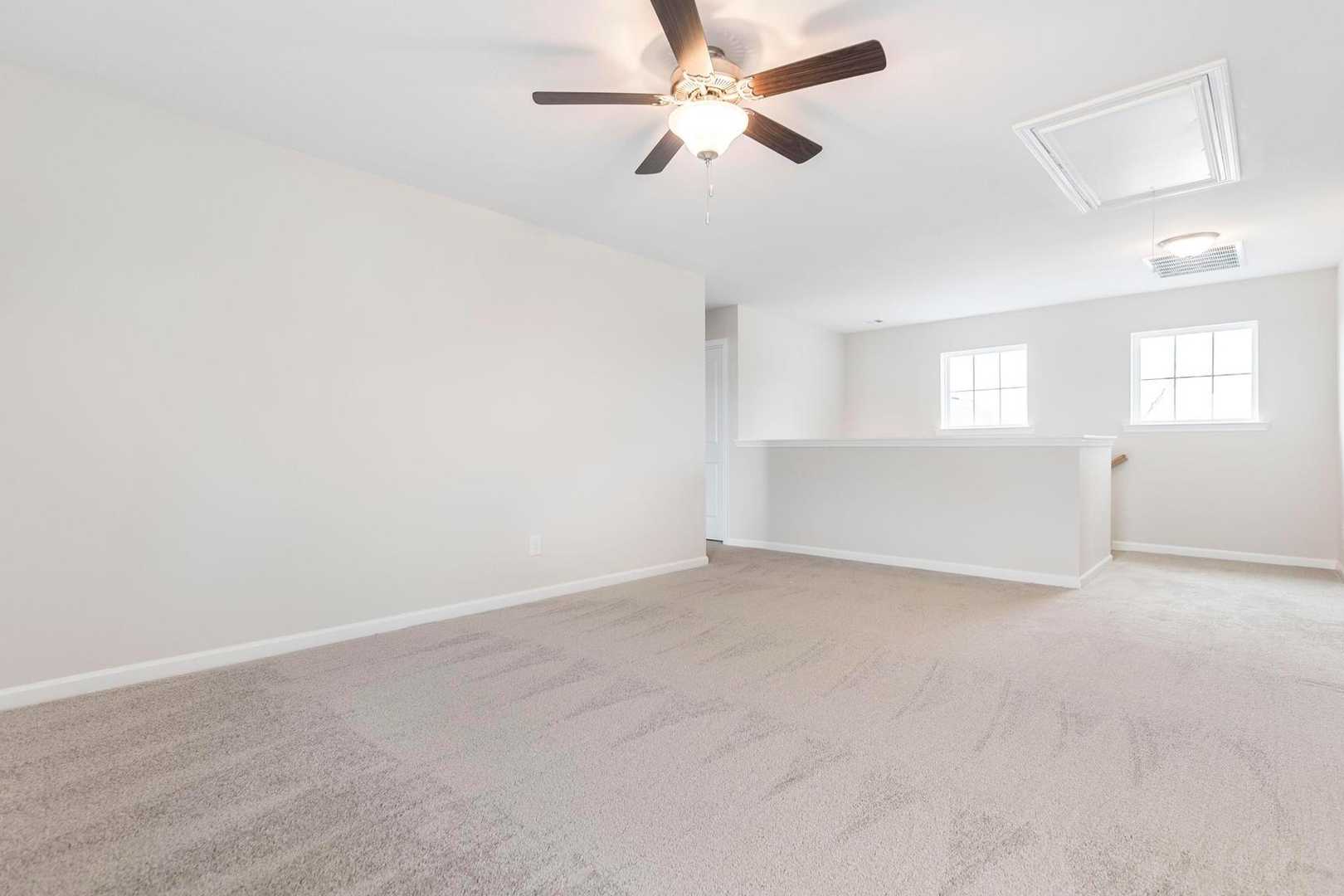 Spacious loft area with ceiling fan, beige carpet, white walls, and side windows at Cape Reserve at Donahue Ridge in Auburn, Alabama