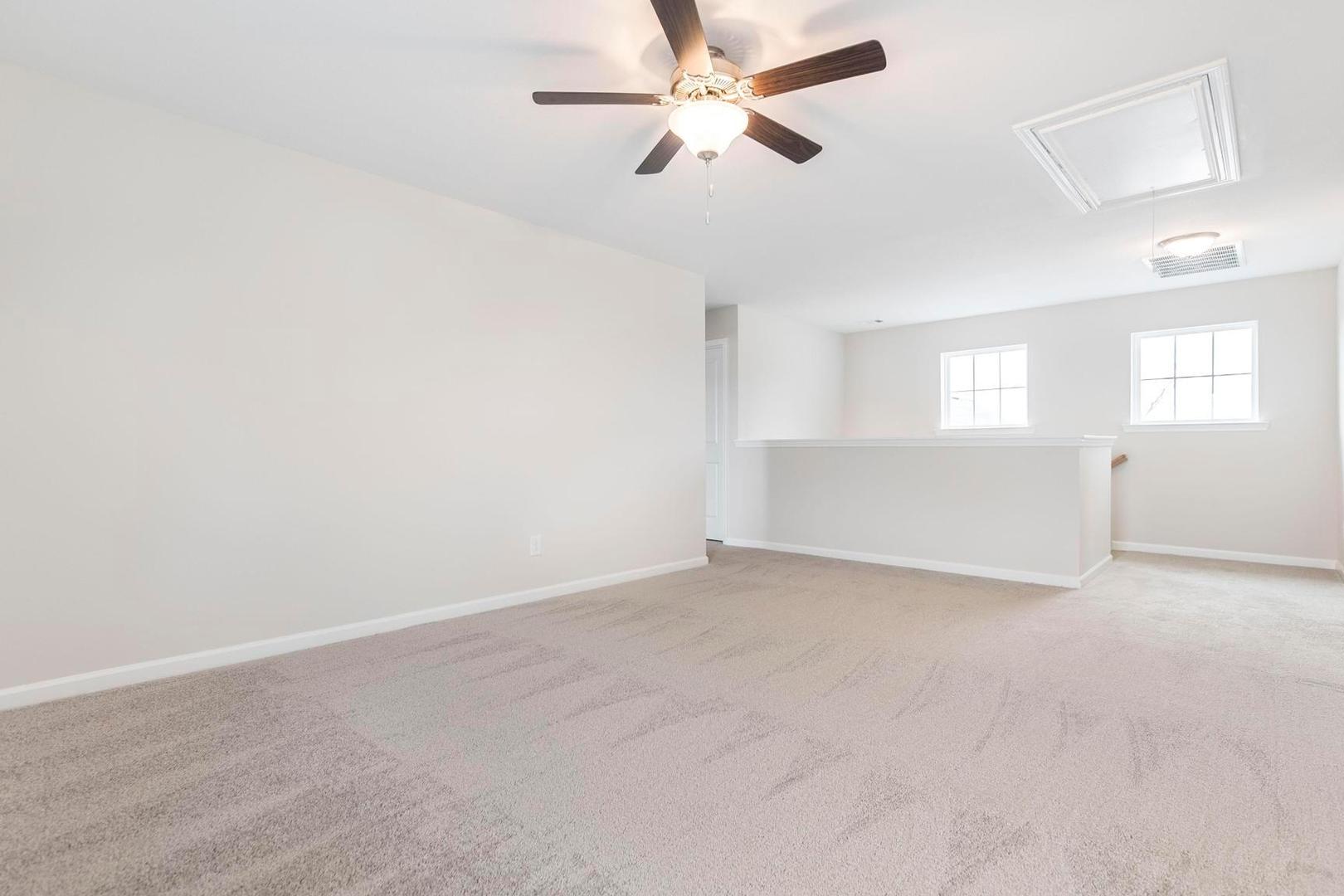 Spacious loft area with ceiling fan, beige carpet, white walls, and side windows at Cape Reserve at Donahue Ridge in Auburn, Alabama