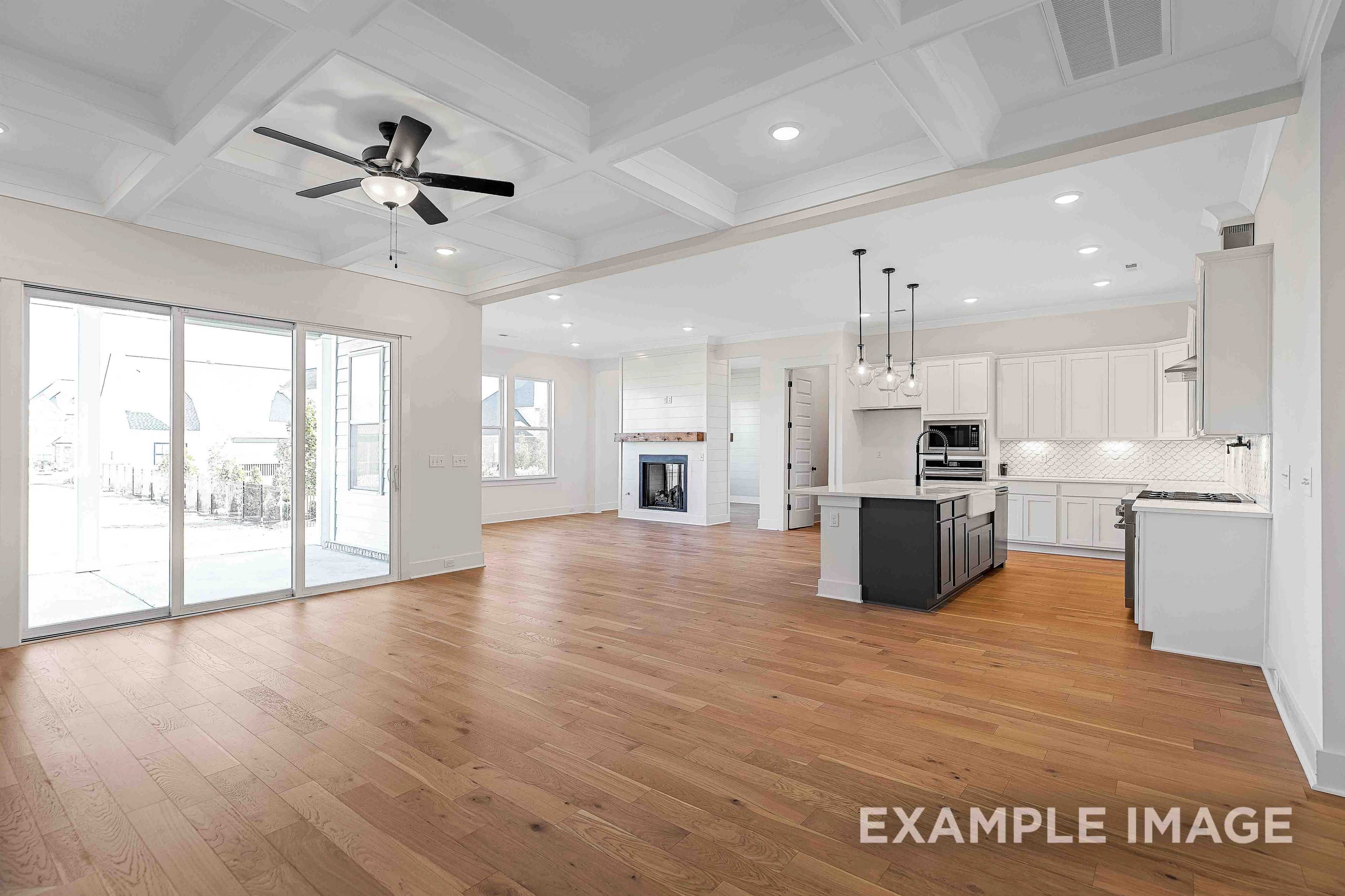 Spacious open-concept kitchen and living area in The Albany A with hardwood floors, white cabinets, black island, and modern fireplace